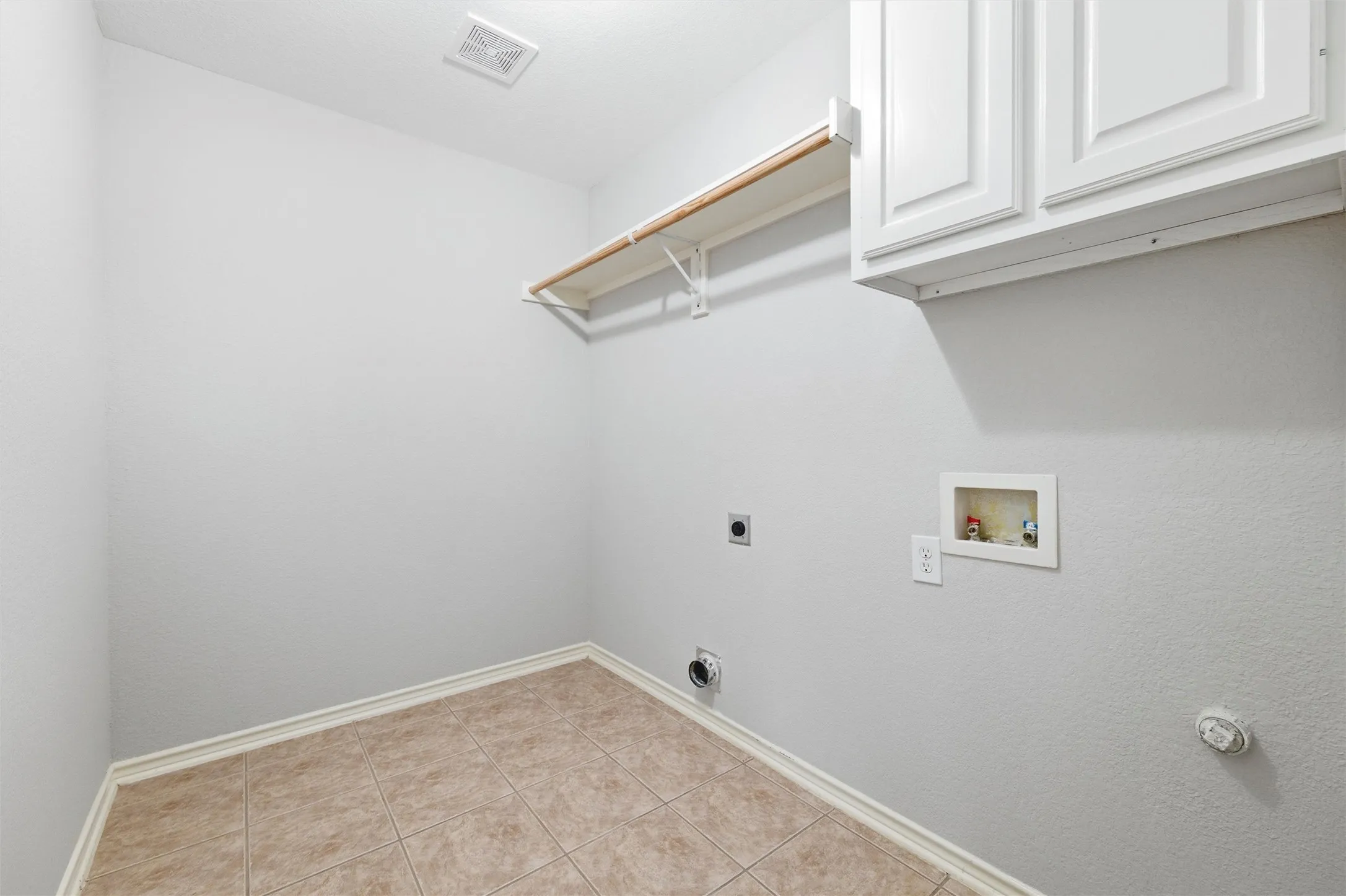 Dedicated laundry room with tile flooring, built-in shelving, and upper cabinetry for convenient storage and organization.