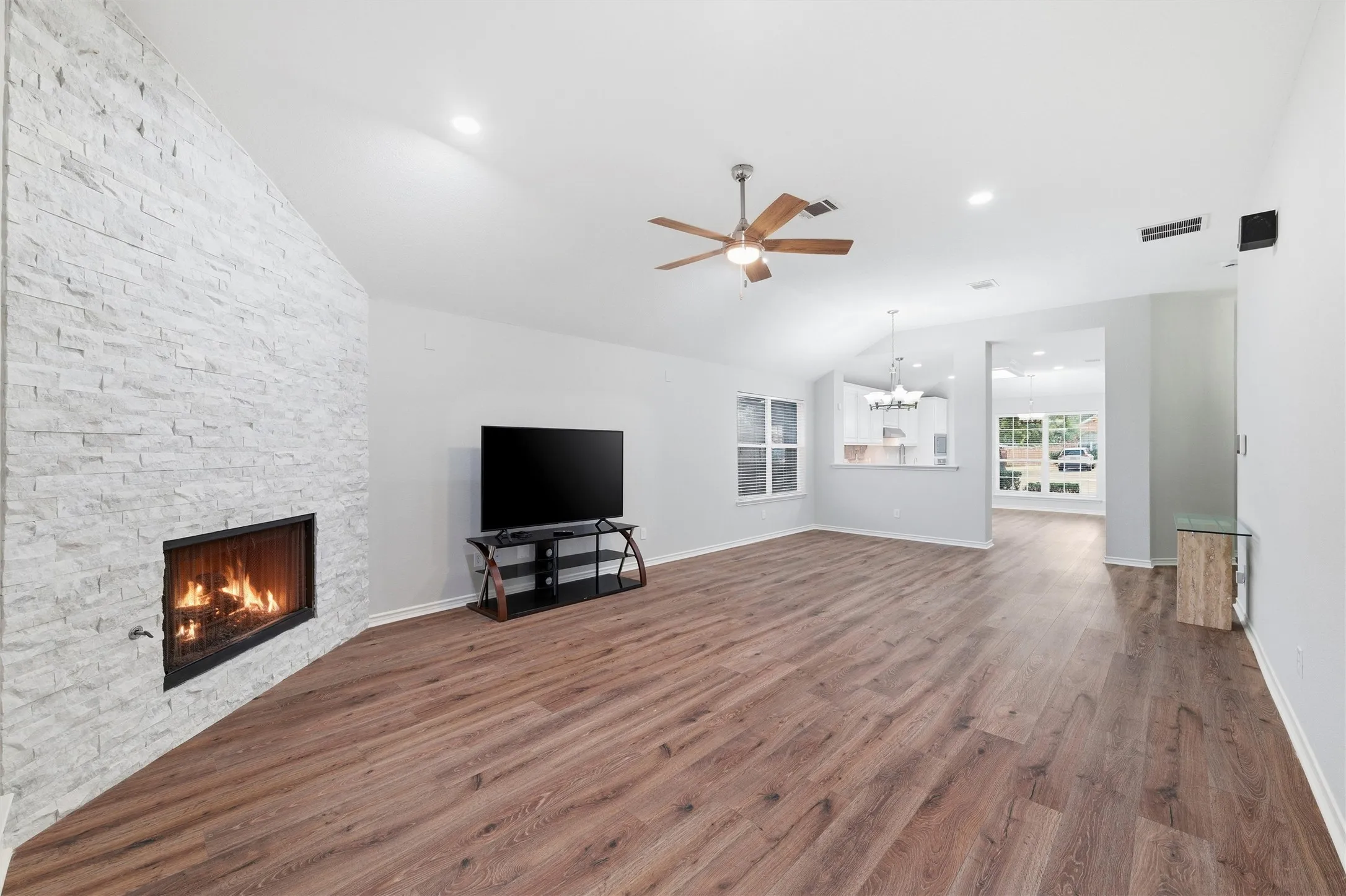 Spacious open-concept living room featuring rich wood-look flooring, soaring ceilings, and a stunning floor-to-ceiling stone fireplace that creates a beautiful focal point year-round.