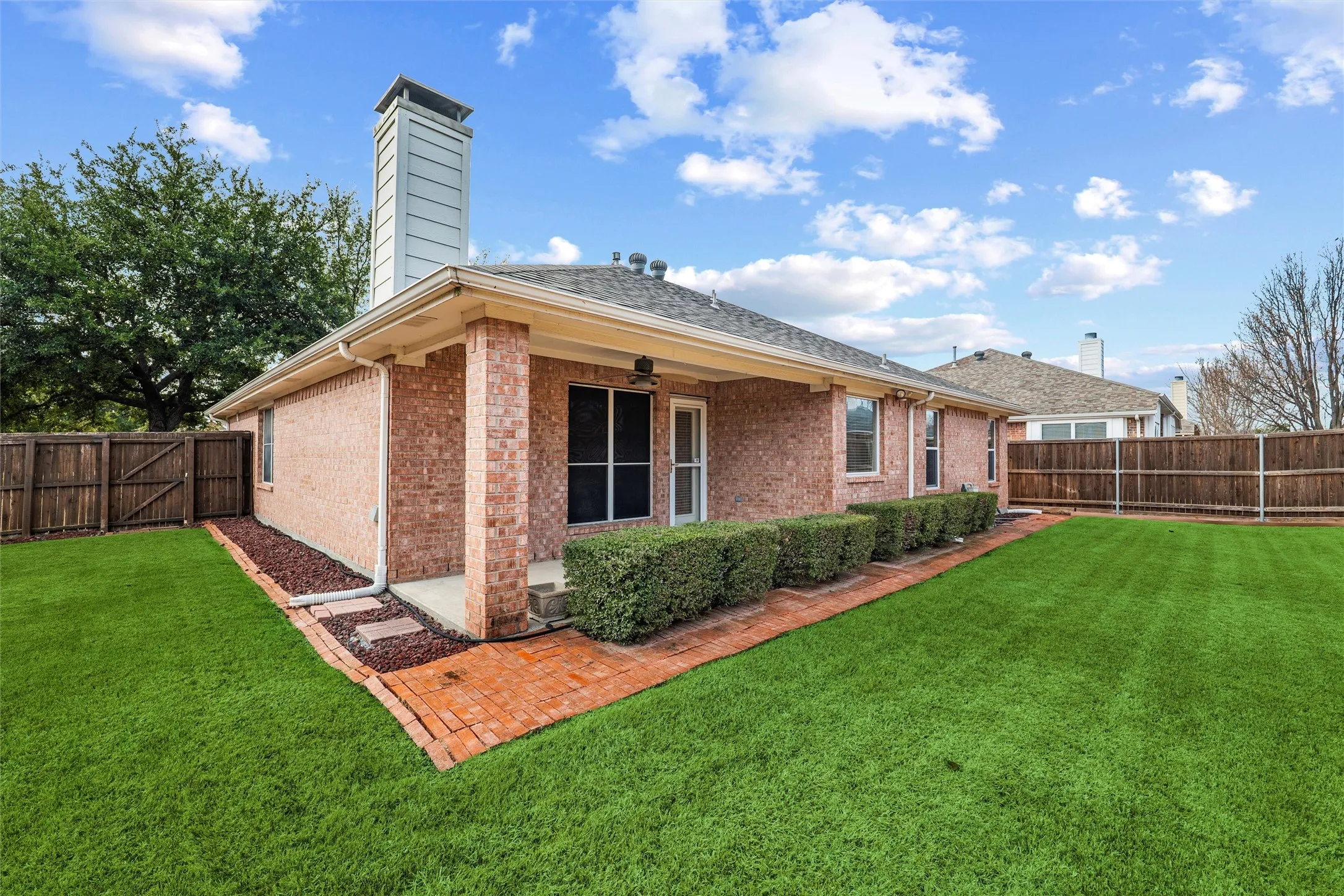 Rear view of the home showcasing the covered patio, privacy fencing, and thoughtfully maintained landscaping.