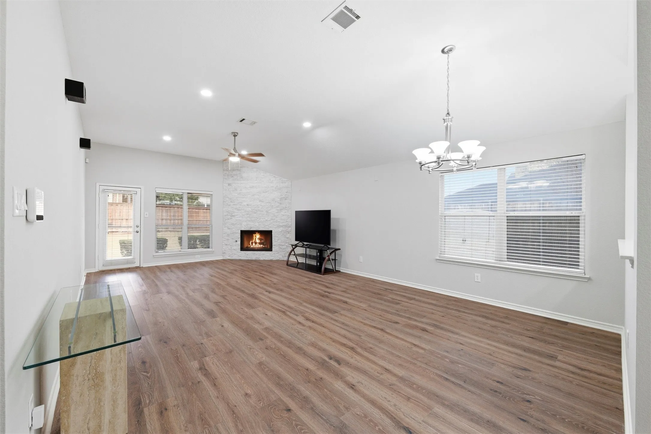 Spacious open living area featuring brand-new LVP flooring, abundant natural light, and a dramatic floor-to-ceiling stone fireplace as the focal point.