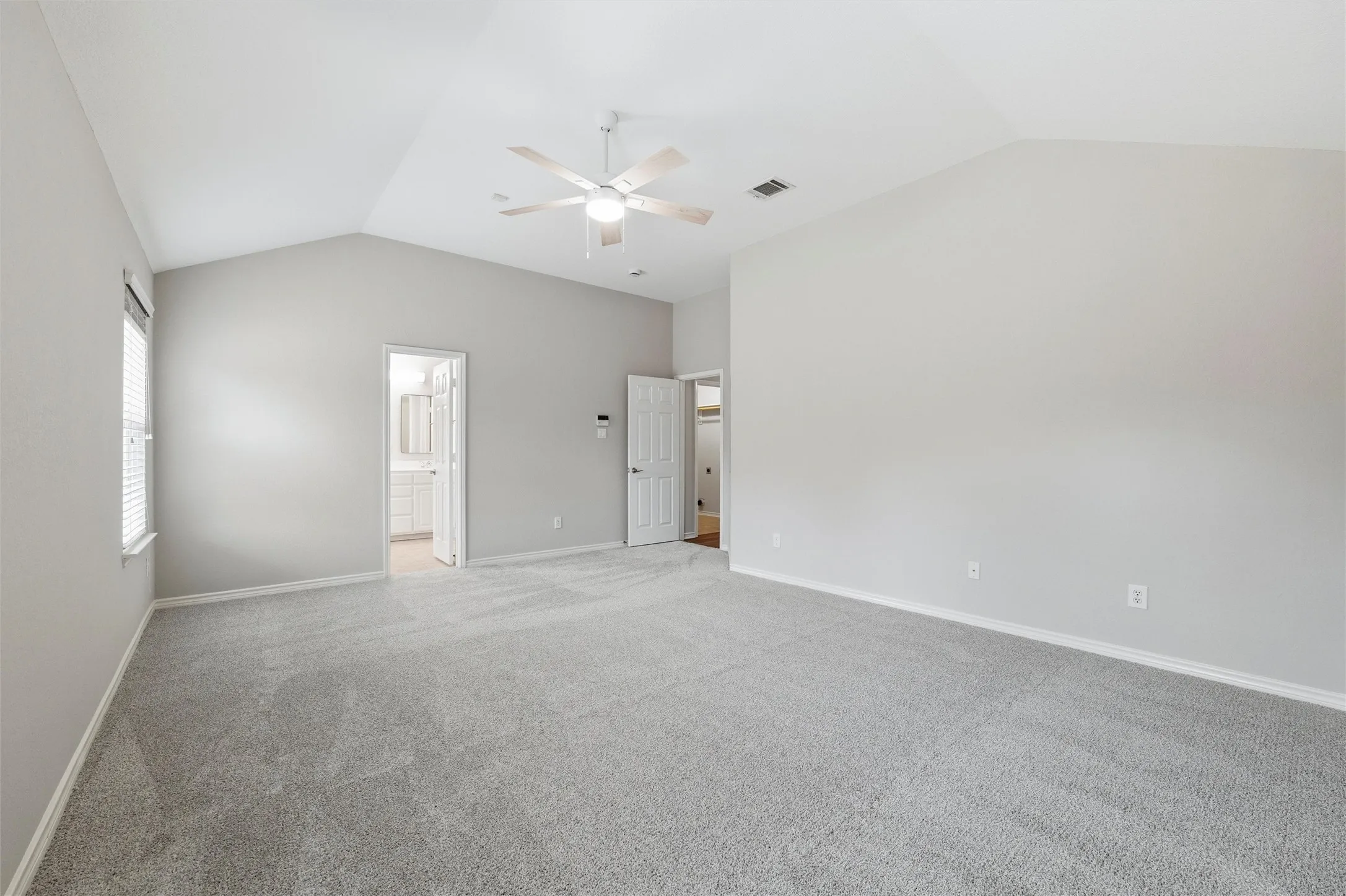 Another view of the primary bedroom highlights the generous room size, neutral color palette, and updated ceiling fan.