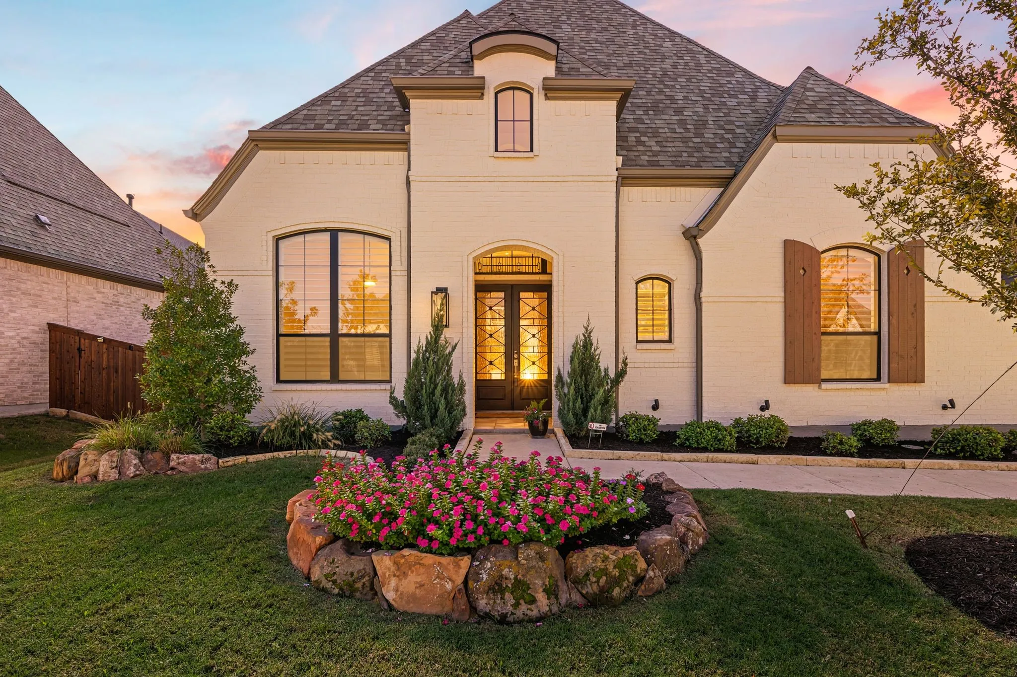 Cream brick exterior with dark shingle roofing, arched windows, and a dark wood entry door with glass inserts