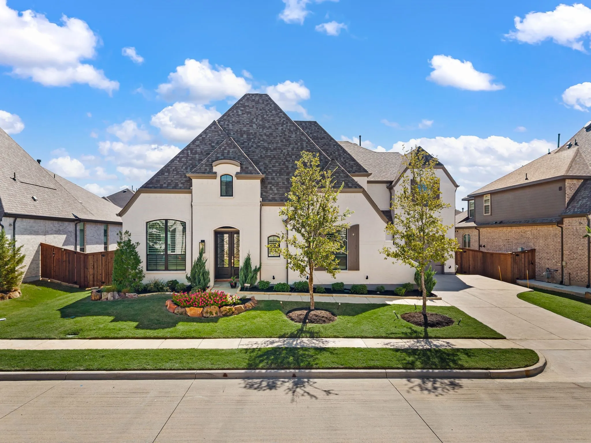 Stucco exterior featuring an arched entryway, dark-frame windows, a gabled roofline, and a concrete driveway