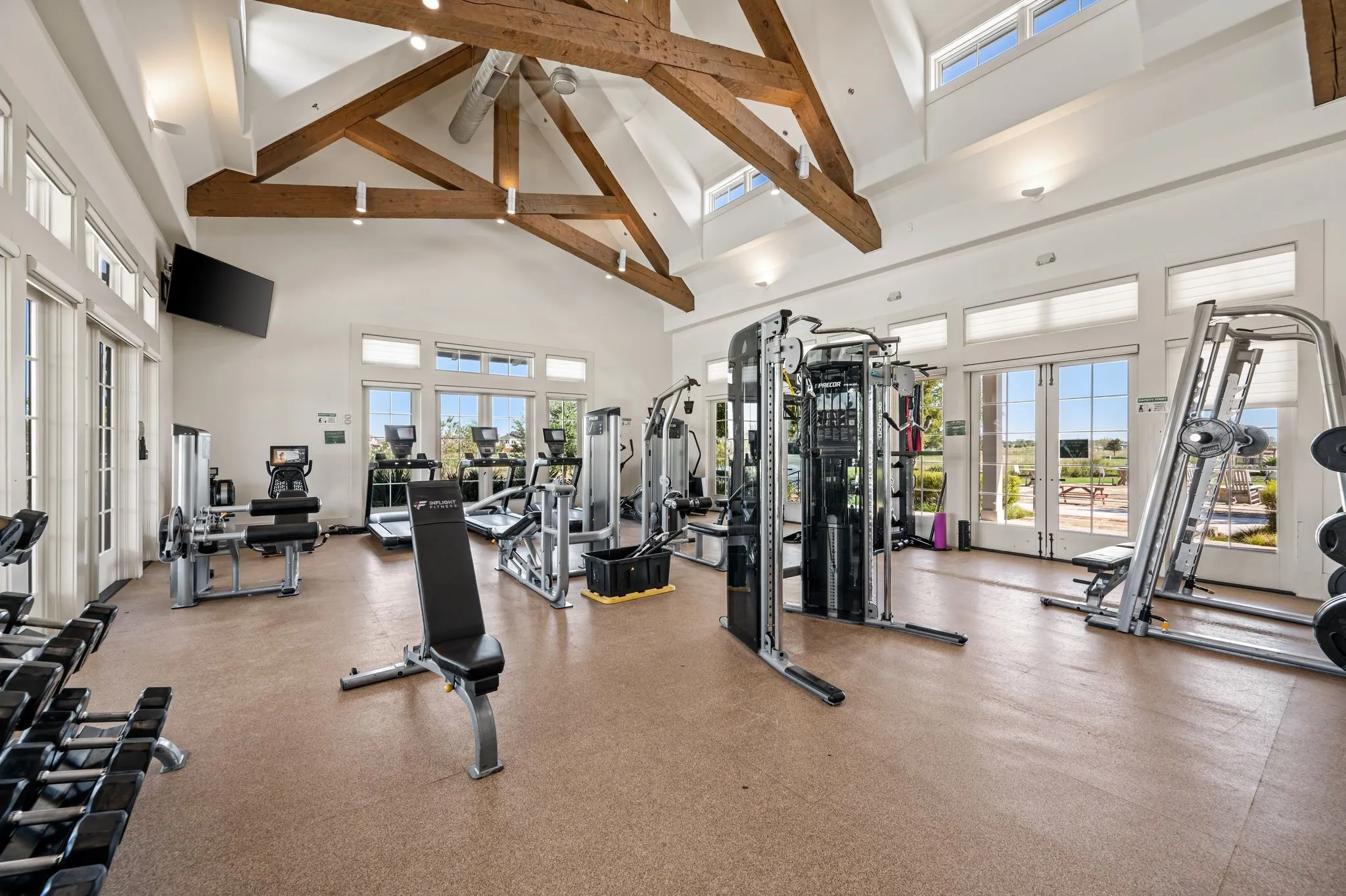 Spacious fitness facility featuring vaulted ceilings with exposed wood beams, ample natural light from large windows, and resilient flooring