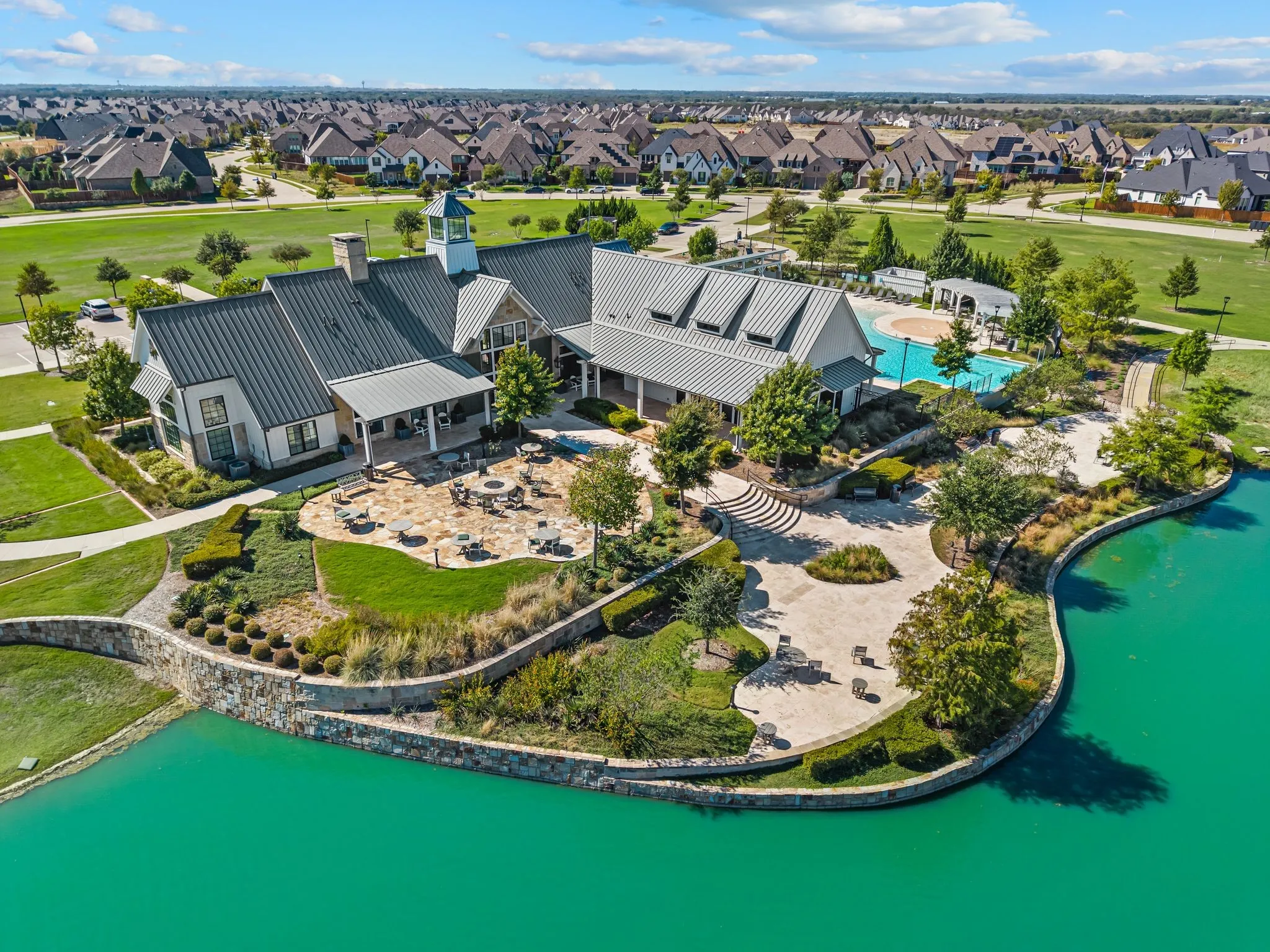 Clubhouse with metal roofing and cupola, expansive patio areas, swimming pool, and stone-edged water feature