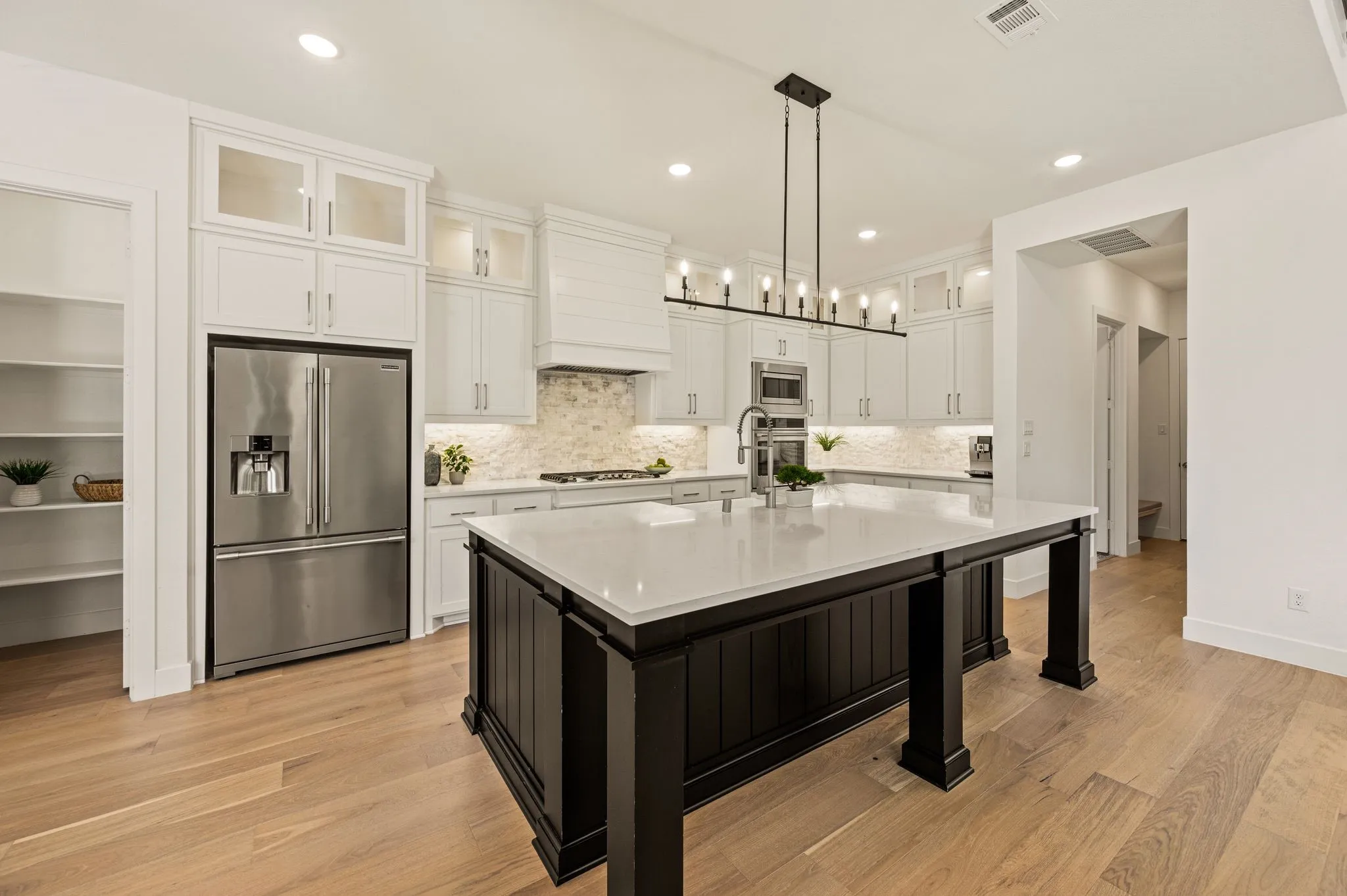 Expansive kitchen featuring a large central island, white cabinetry with glass-front accents, stainless steel appliances, and wood-finish flooring