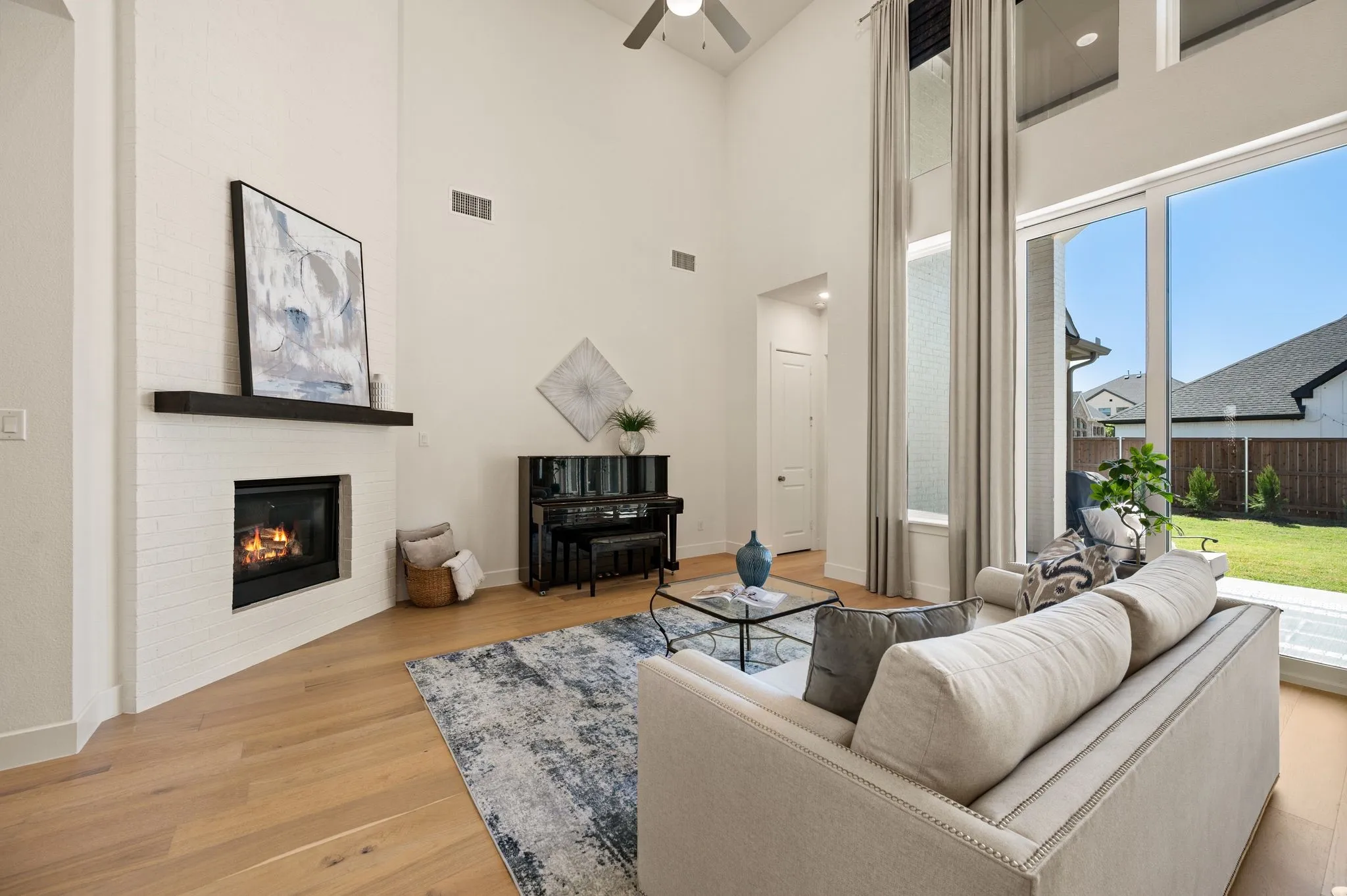 Soaring ceilings, fireplace with a dark wood-finish mantel, wood-finish flooring, expansive sliding glass doors, and a manicured lawn