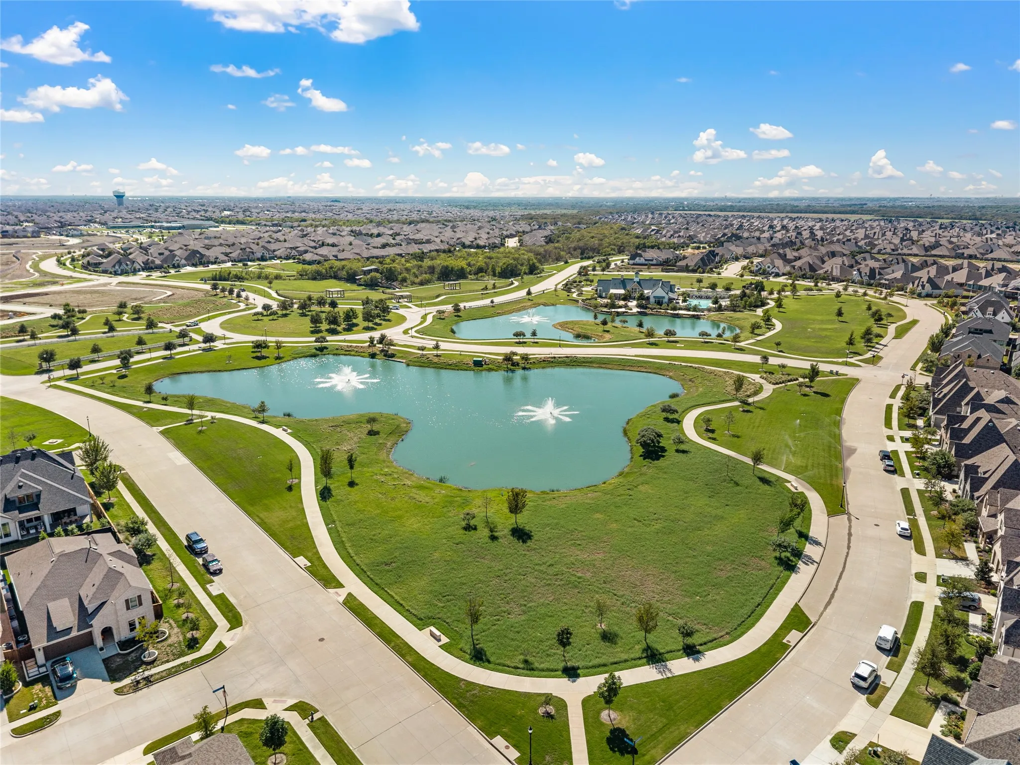 Expansive community green space featuring multiple ponds with water features, winding pedestrian pathways, and a large open lawn area