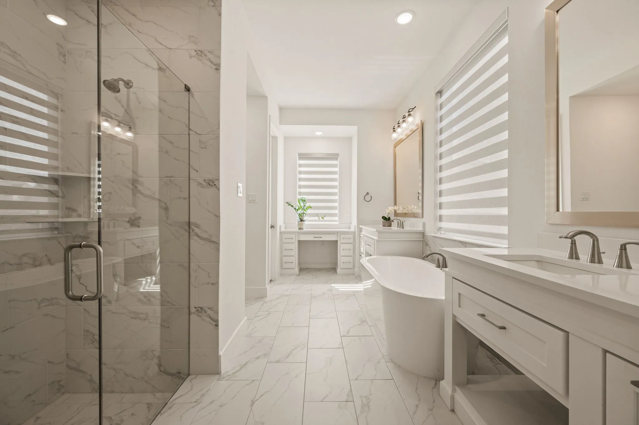 Spacious bathroom featuring a glass-enclosed shower with tiled walls, a freestanding soaking tub, dual vanity with undermount sinks, and a built-in makeup vanity