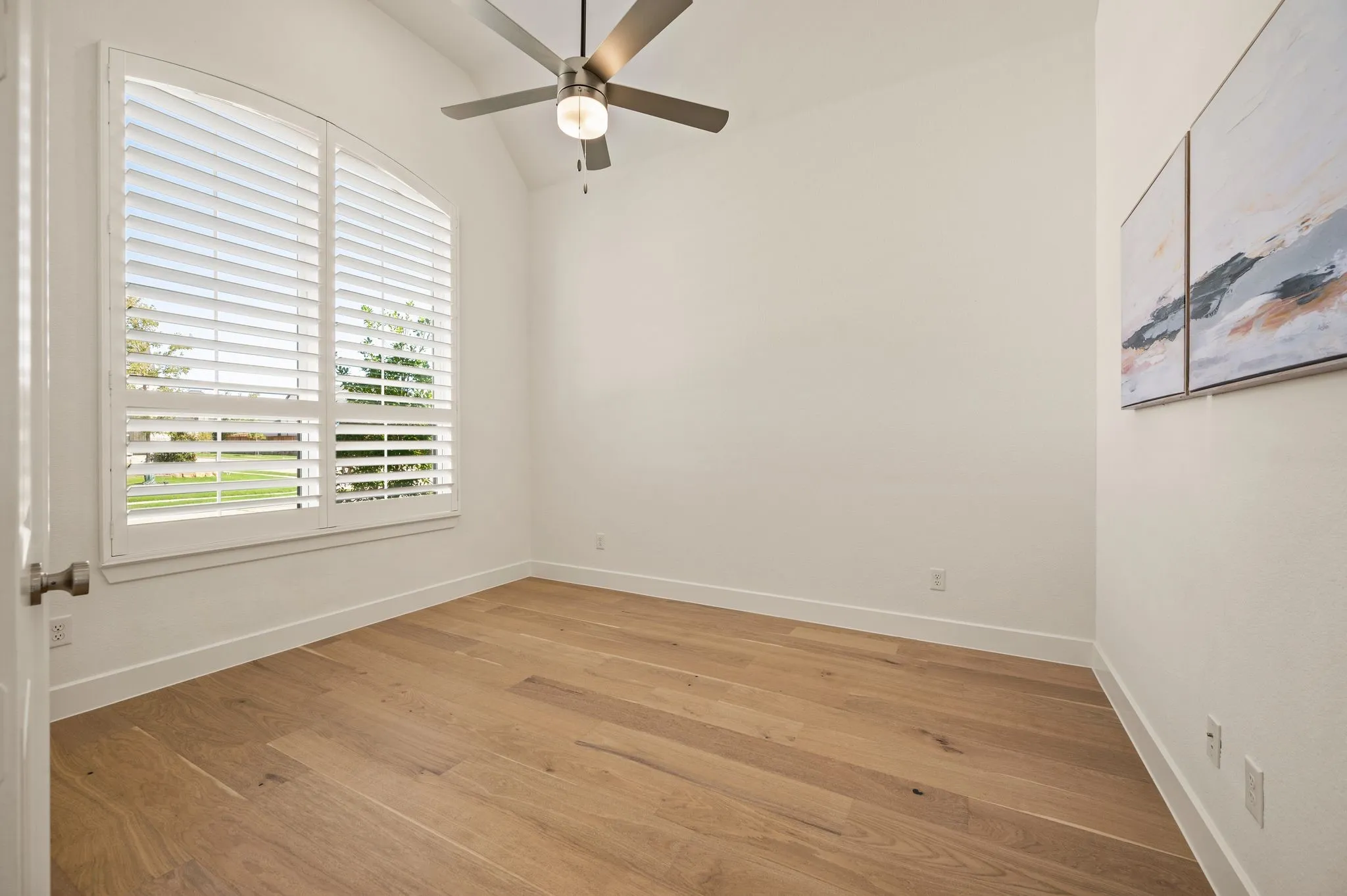 Vaulted ceiling with a ceiling fan, wood-finish flooring, and arched window with plantation shutters