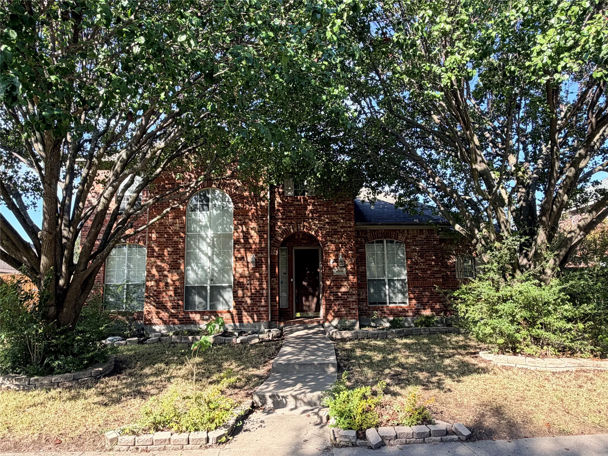 Charming brick residence featuring a classic single-story design with mature tree landscaping, manicured front lawn, and defined hardscape borders