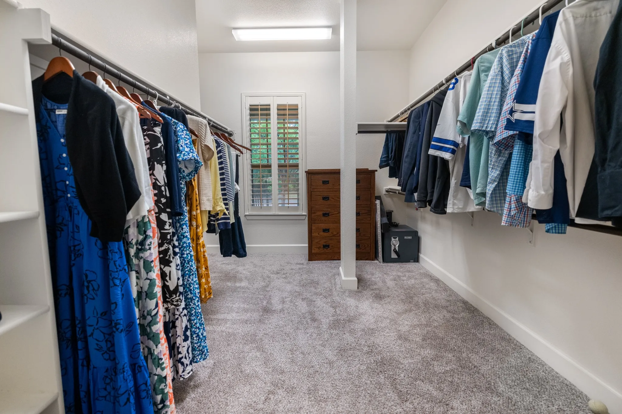 Wall-to-wall carpeting, multiple hanging rods, built-in shelving, white plantation shutters, and a recessed ceiling light fixture