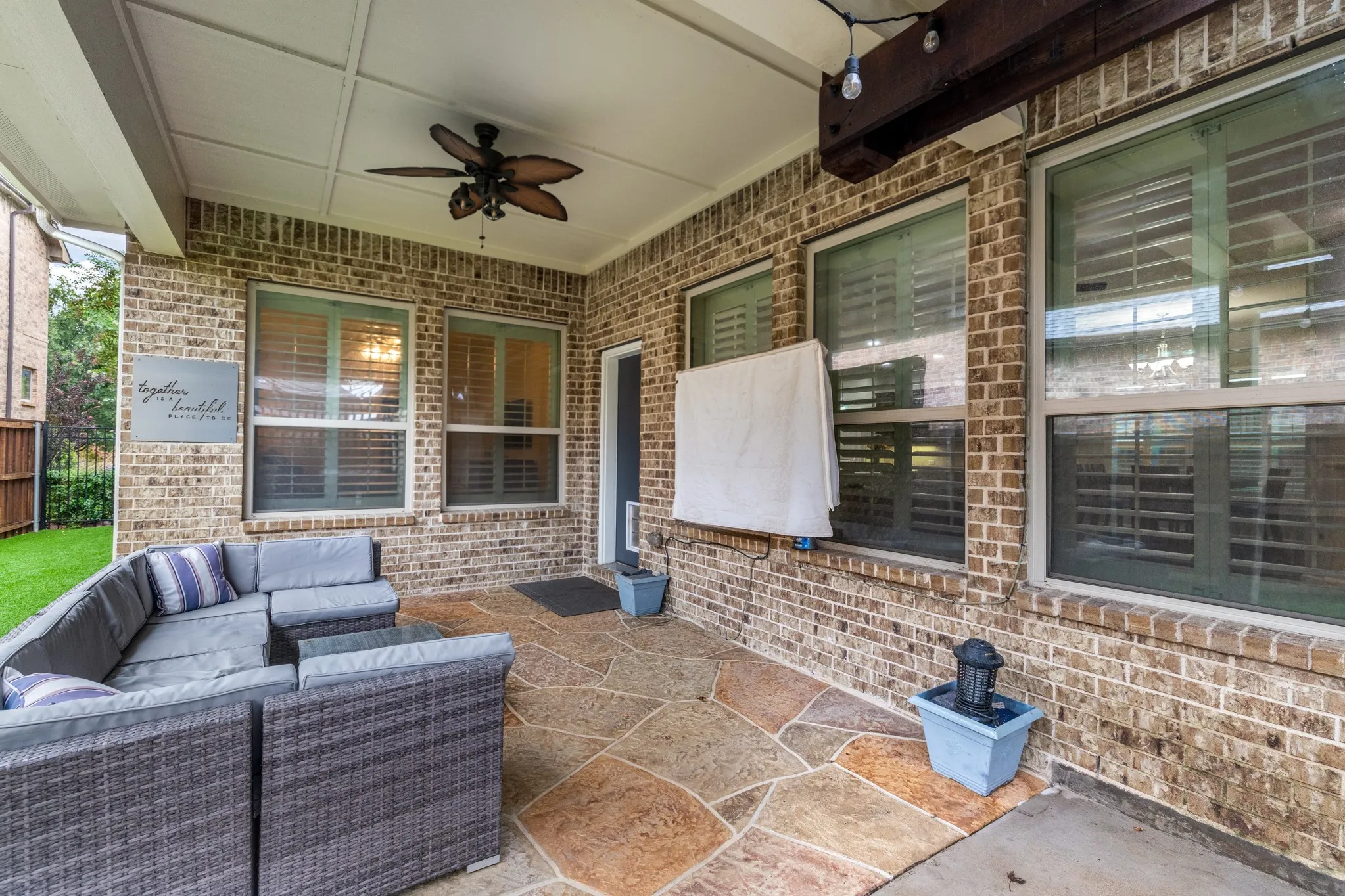 Covered patio featuring a ceiling fan, brick exterior, flagstone-style flooring, and multiple windows with blinds