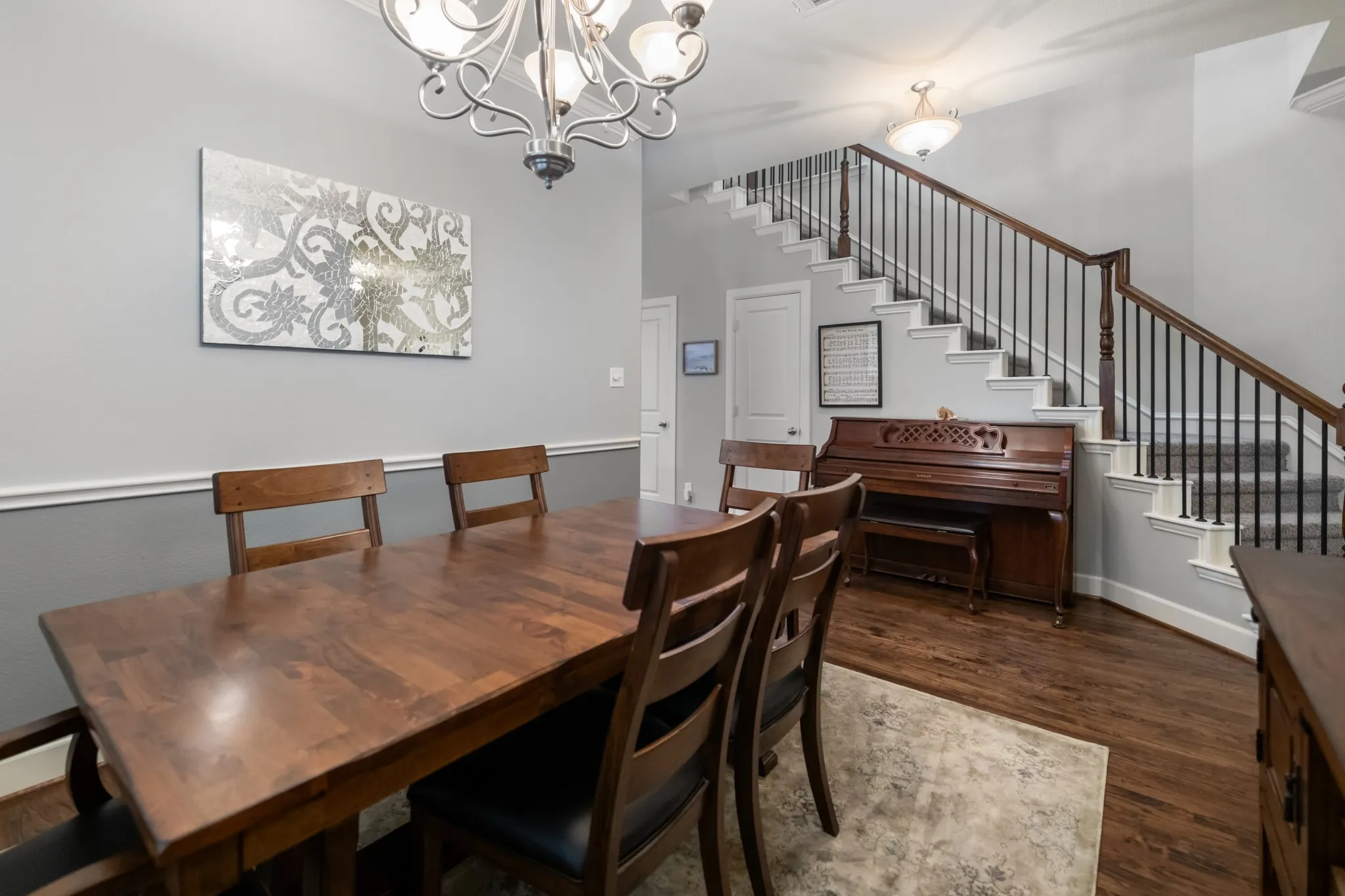 Wood-finish flooring, staircase with dark wood handrail and black iron balusters, two-tone wall with chair rail, chandelier lighting, and recessed ceiling light fixtures