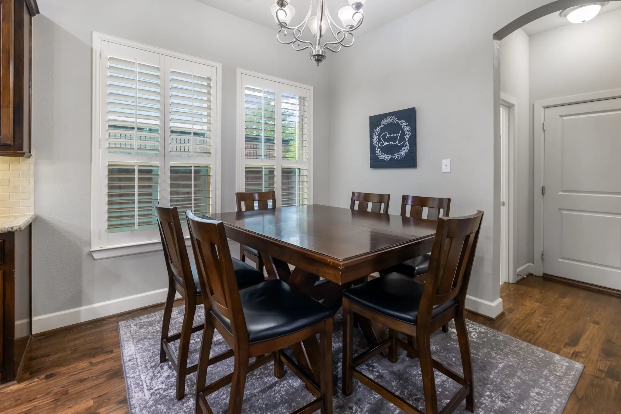 Two windows with plantation shutters, wood-finish flooring, and an arched entry
