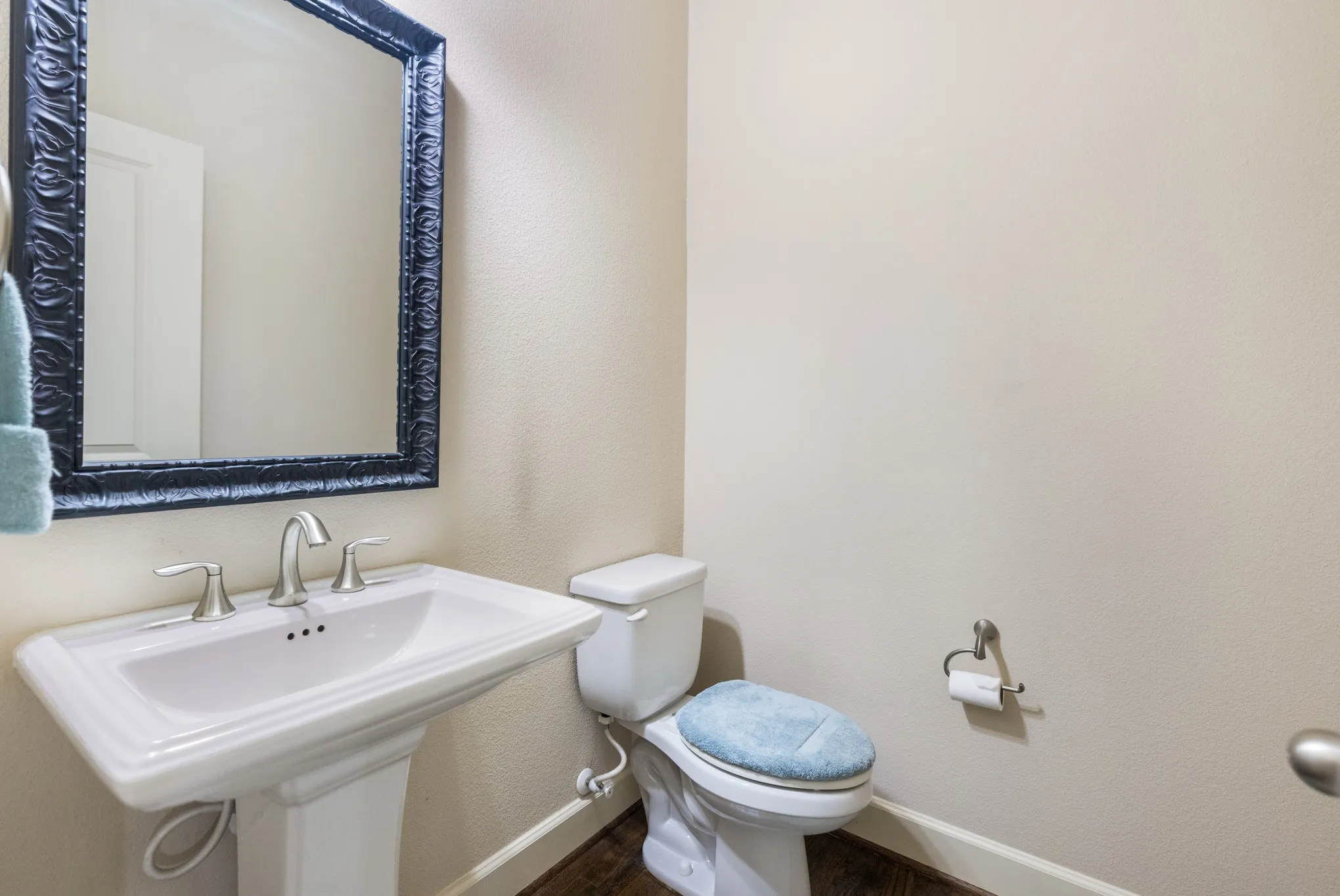 Downstairs powder room with pedestal sink with dual-handle faucet, ornate framed mirror, and wood-finish flooring