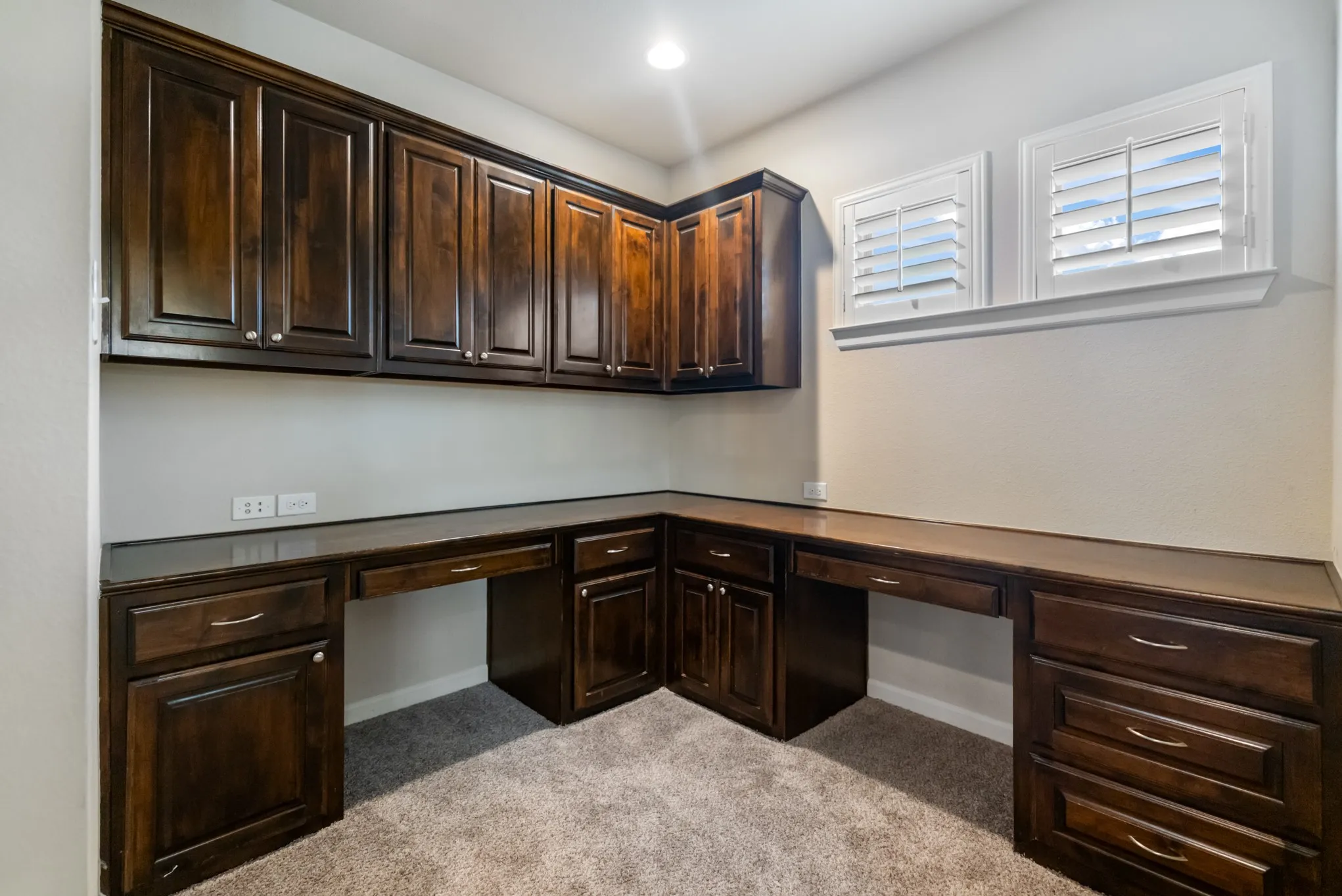 Upstairs. Built-in desk with dark wood-finish cabinetry, ample storage, and two windows featuring white plantation shutters