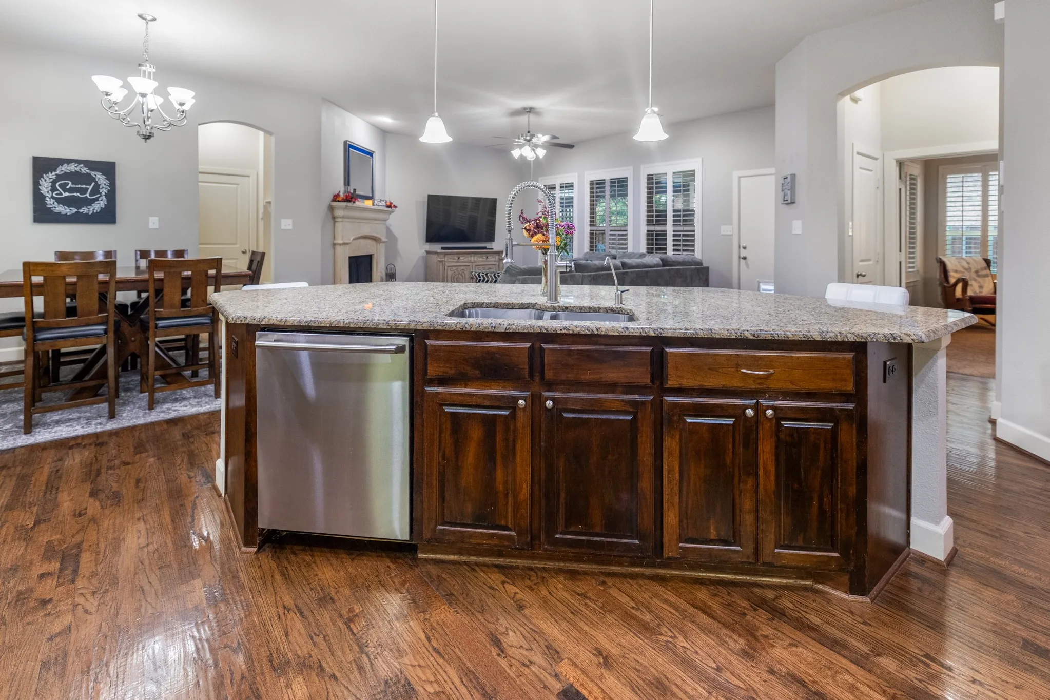 Expansive kitchen island with a granite countertop, built-in stainless steel dishwasher, and rich wood cabinetry