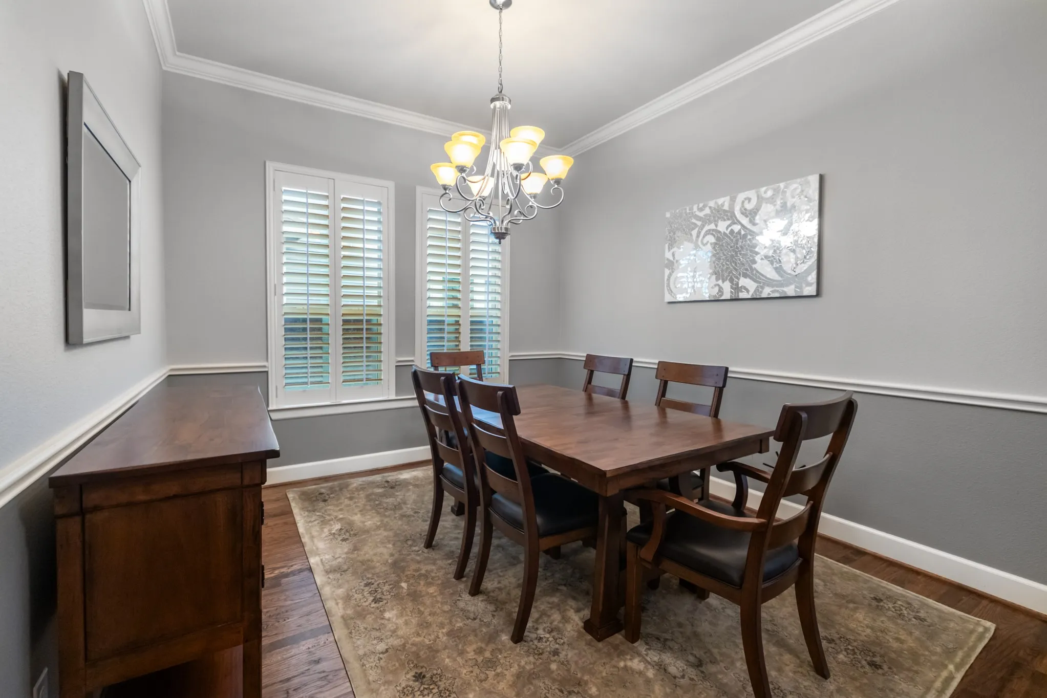 Hardwood flooring, elegant crown molding, chair rail detailing, plantation shutters, and a classic chandelier