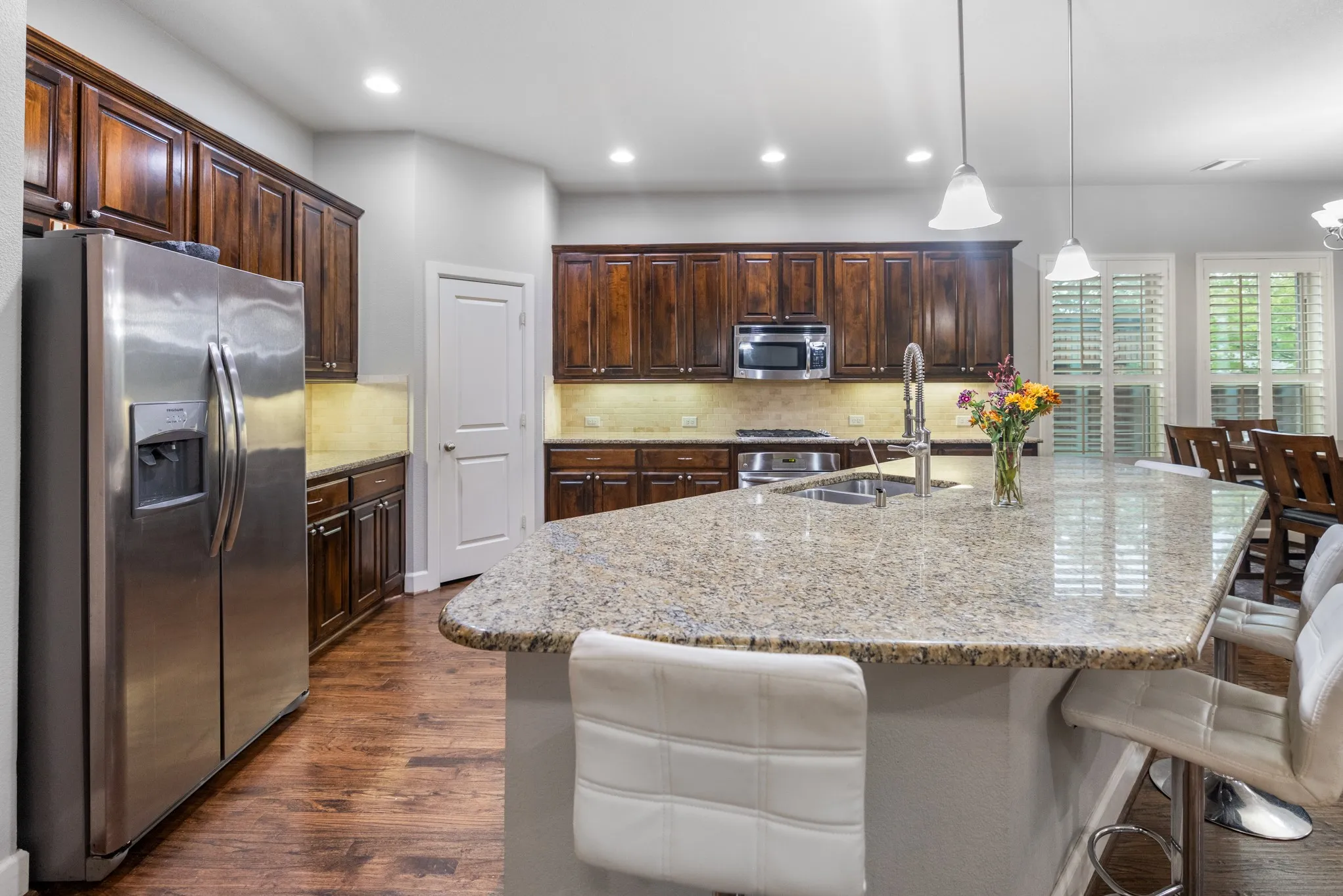 Kitchen featuring a large island with stone countertops, wood-finish flooring, stainless steel appliances, dark wood cabinetry, and recessed lighting