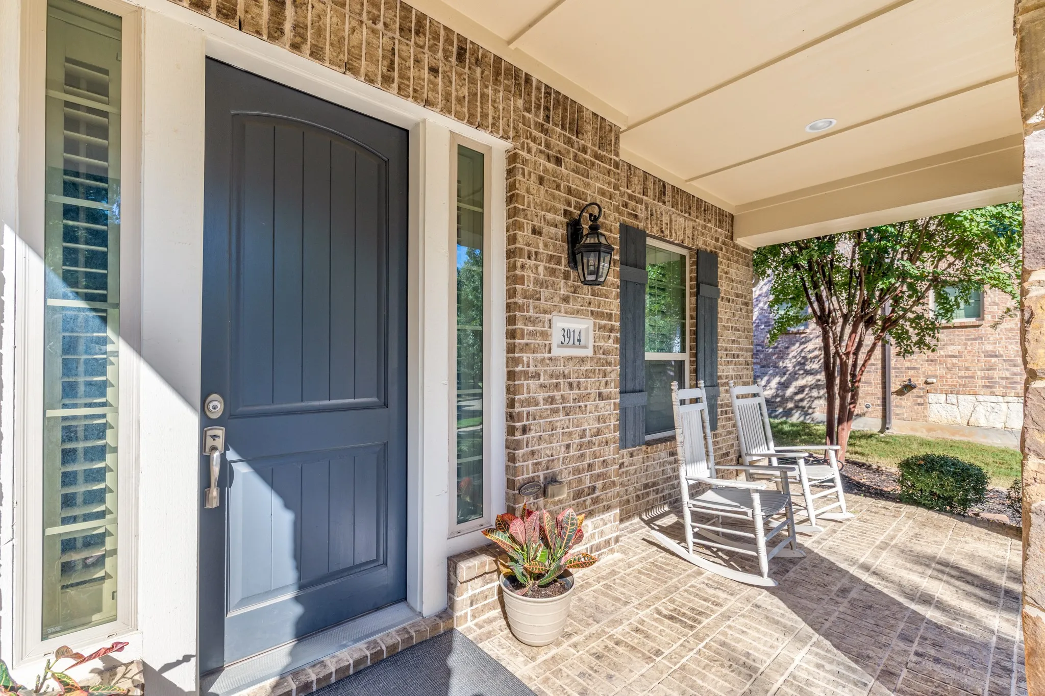 Covered front porch and door. Brick exterior, featuring a dark blue entry door with sidelights, and a wall-mounted light fixture