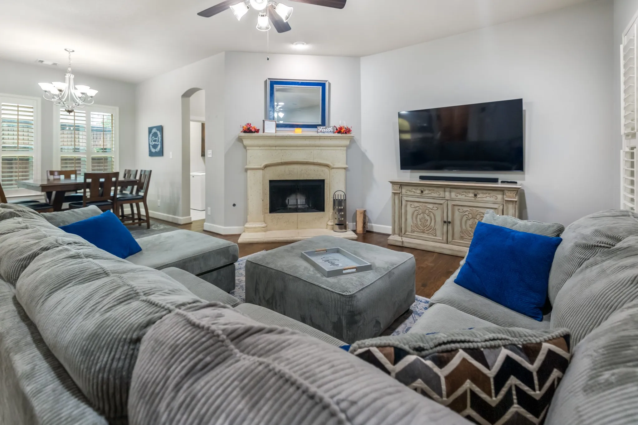 Living area with wood-finish flooring, a stone-surround fireplace, and a ceiling fan
