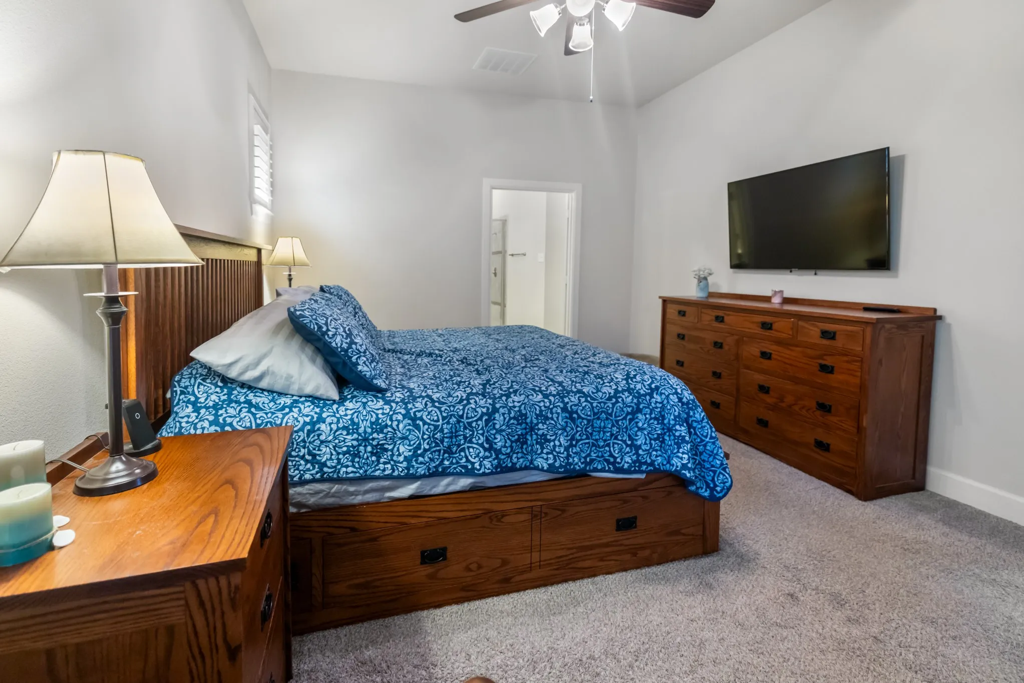Vaulted ceiling featuring a ceiling fan with integrated lighting, wood-finish headboard, and soft gray carpeting