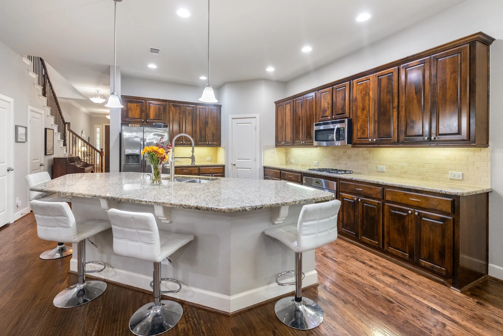 Spacious kitchen featuring an expansive island with a granite countertop, wood-finish flooring, dark wood cabinetry, a stainless steel refrigerator, and a built-in microwave