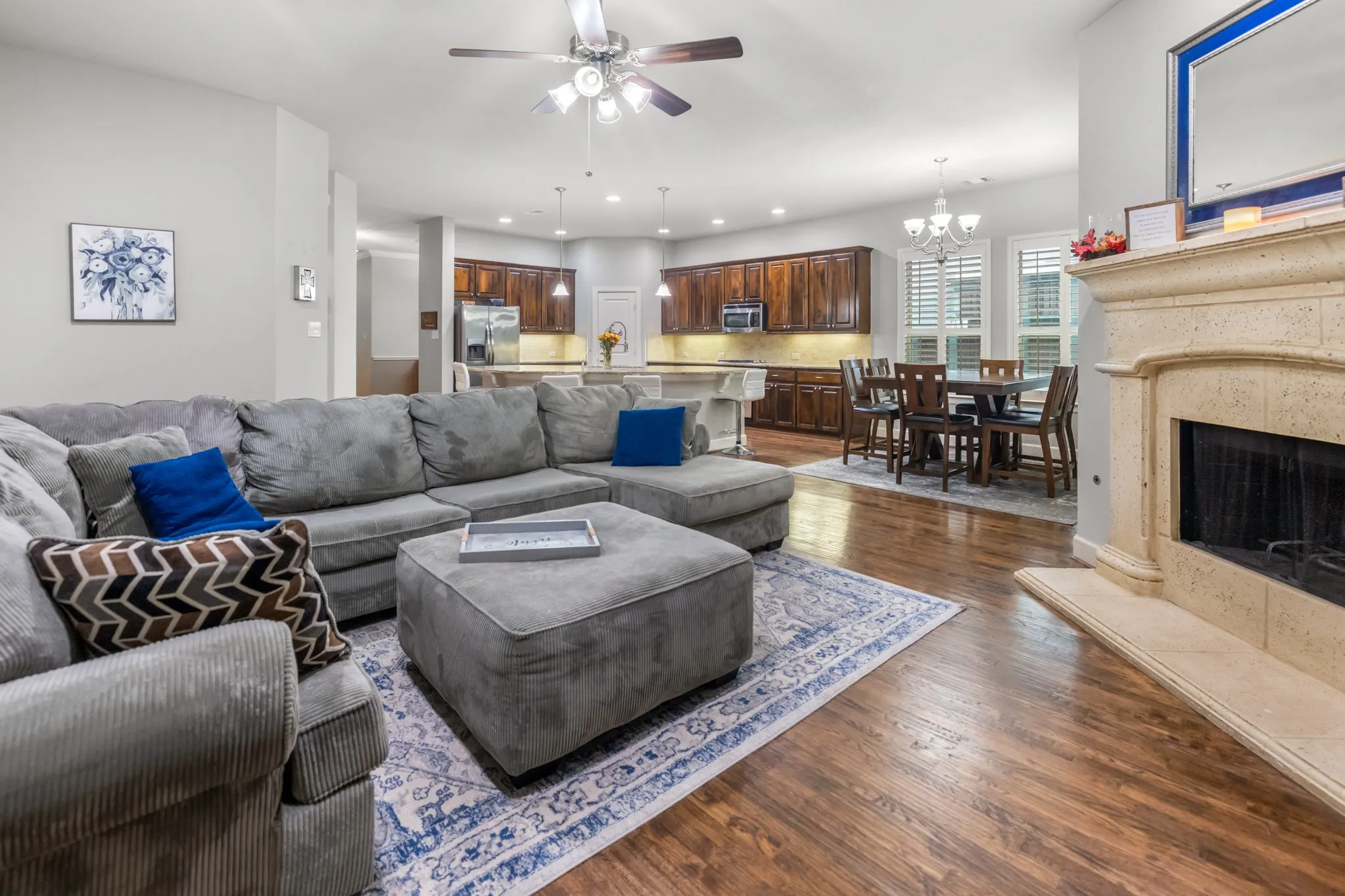 Hardwood-finish flooring throughout, ceiling fan with integrated lighting, built-in fireplace with stone surround, kitchen with recessed lighting and under-cabinet lighting, and dining area with chandelier