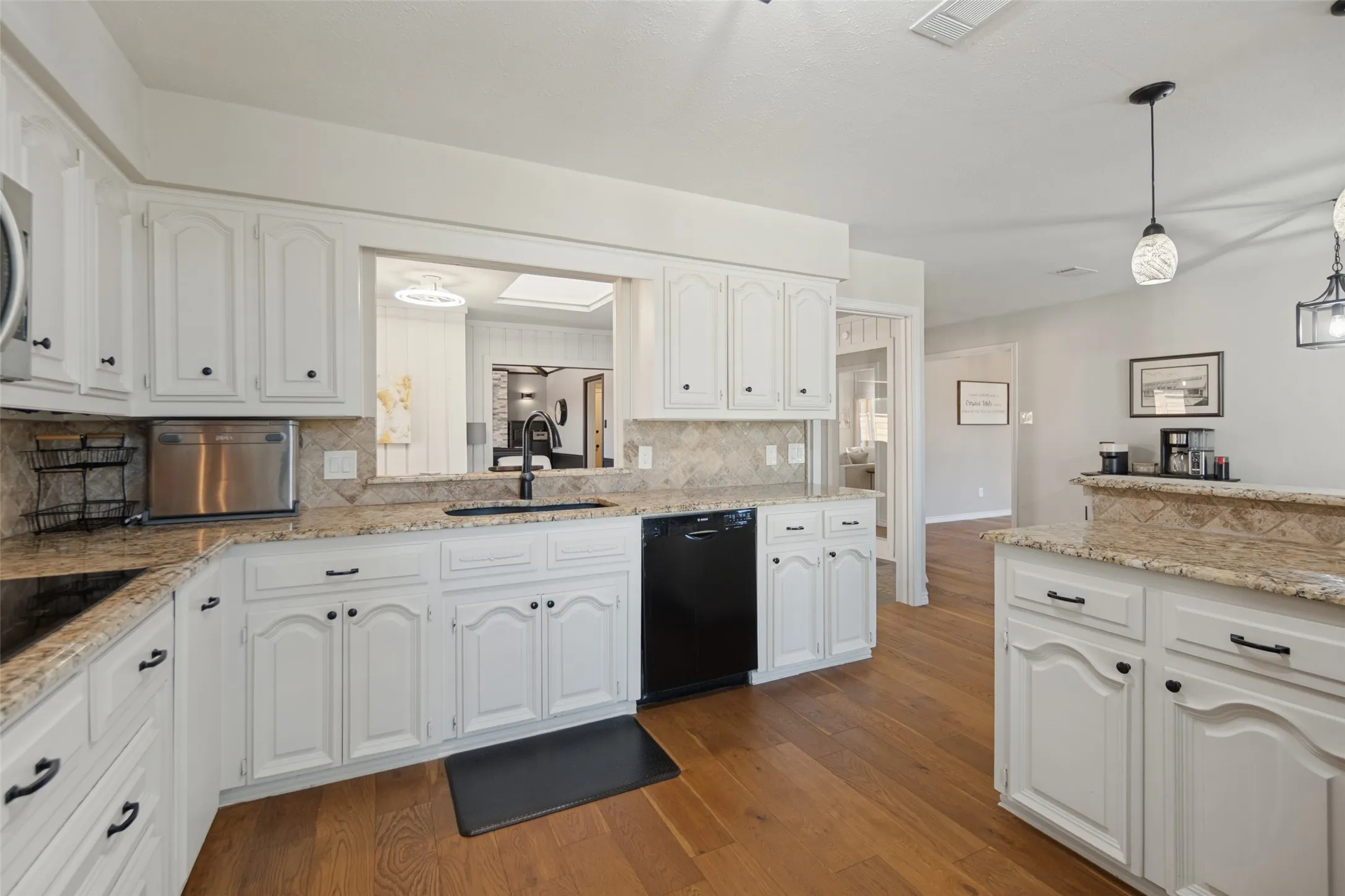 Kitchen featuring white cabinetry, granite countertops, tile backsplash, wood-finish flooring, and a pass-through window
