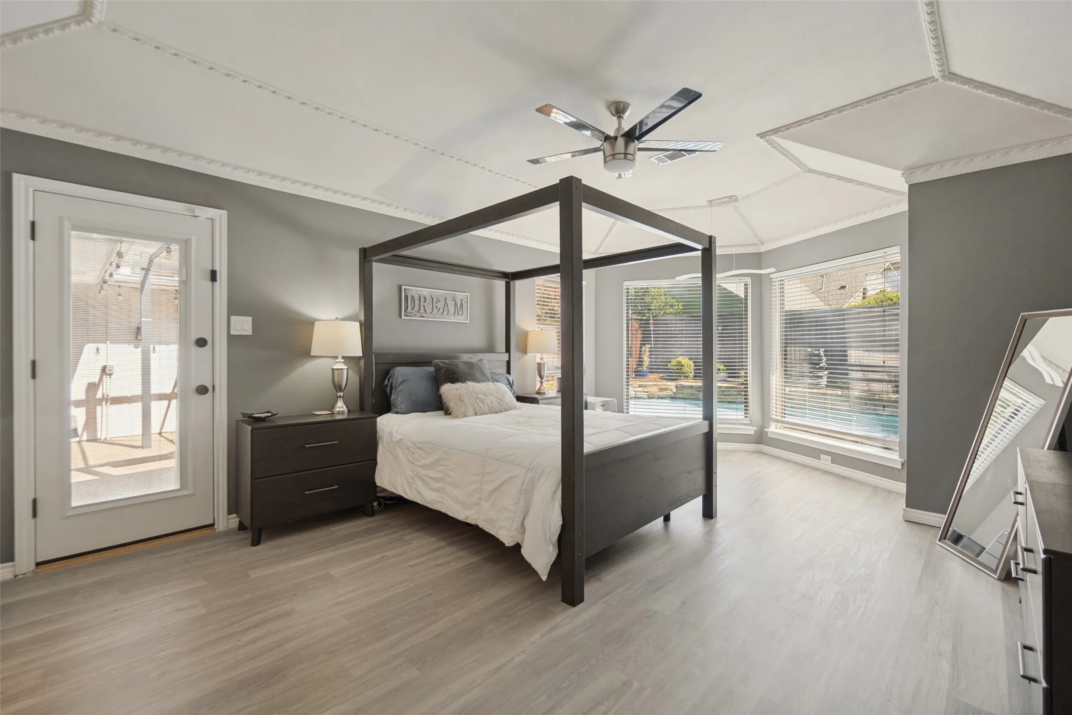 Tray ceiling with decorative molding, ceiling fan, wood-finish flooring, and bay windows