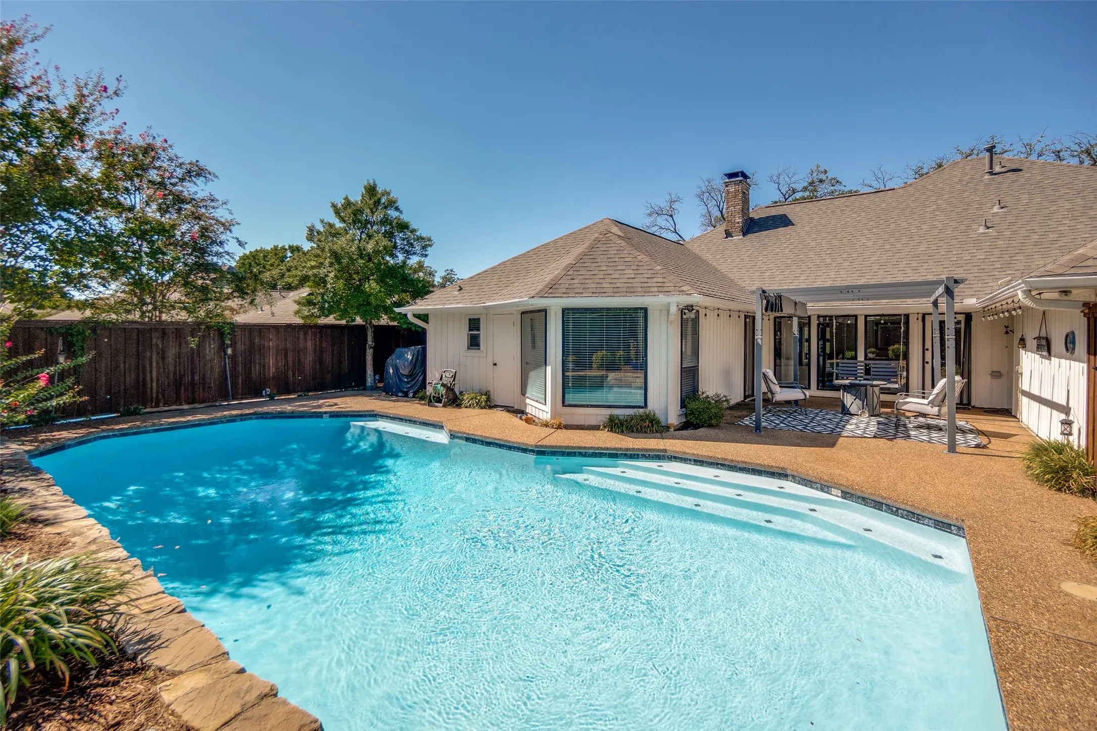 Expansive backyard featuring a clear water swimming pool, stone coping, and a textured concrete patio