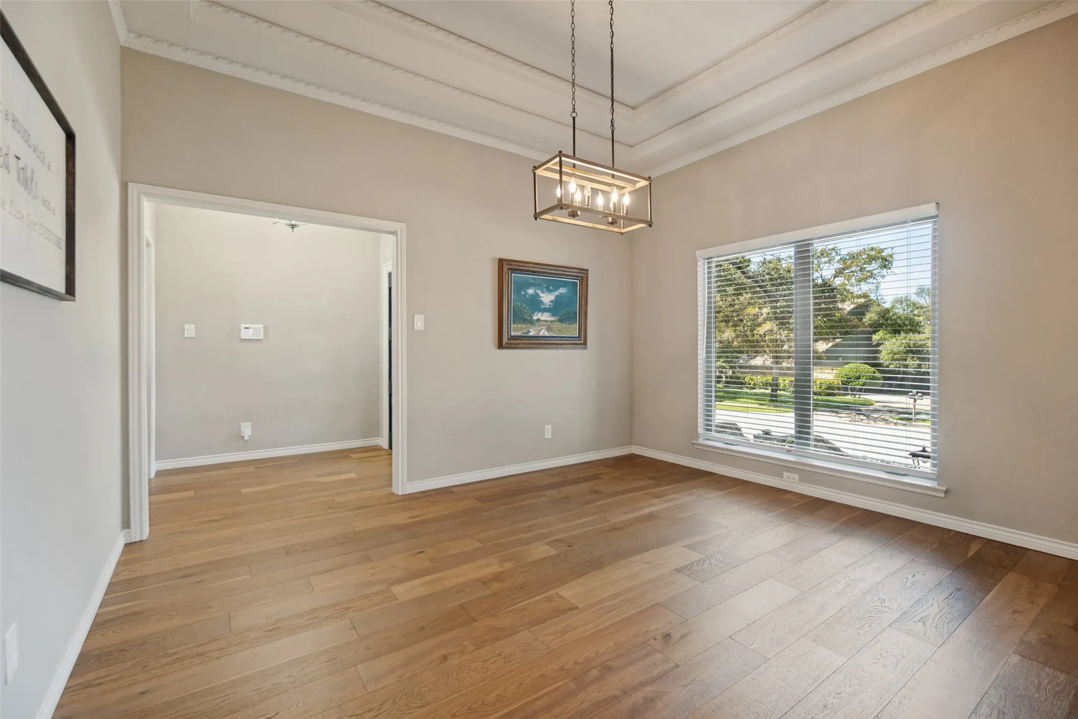 Tray ceiling with crown molding, wood-finish flooring, rectangular window, and a linear chandelier