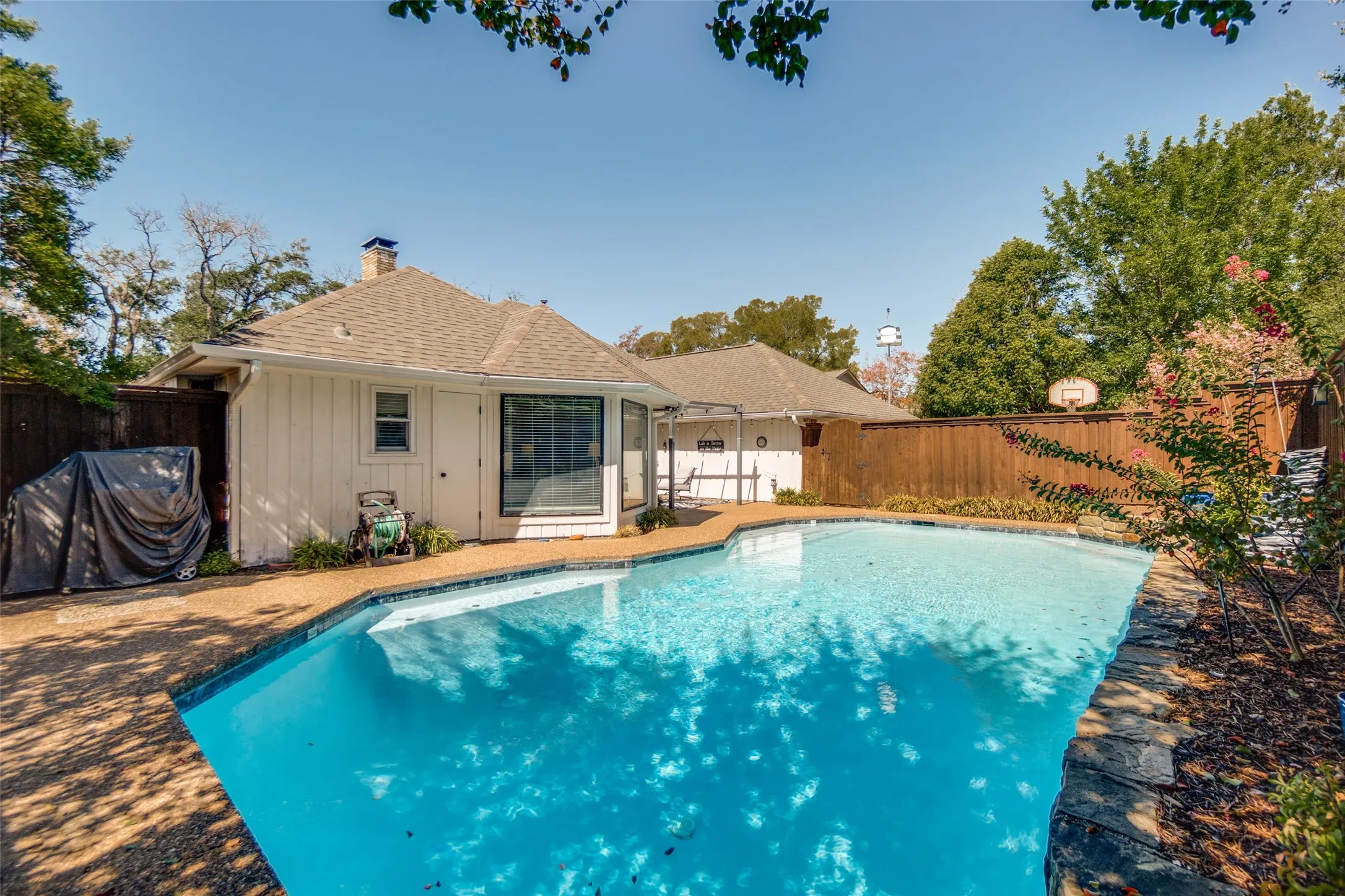 Outdoor swimming pool with concrete decking, wood privacy fence, and mature trees