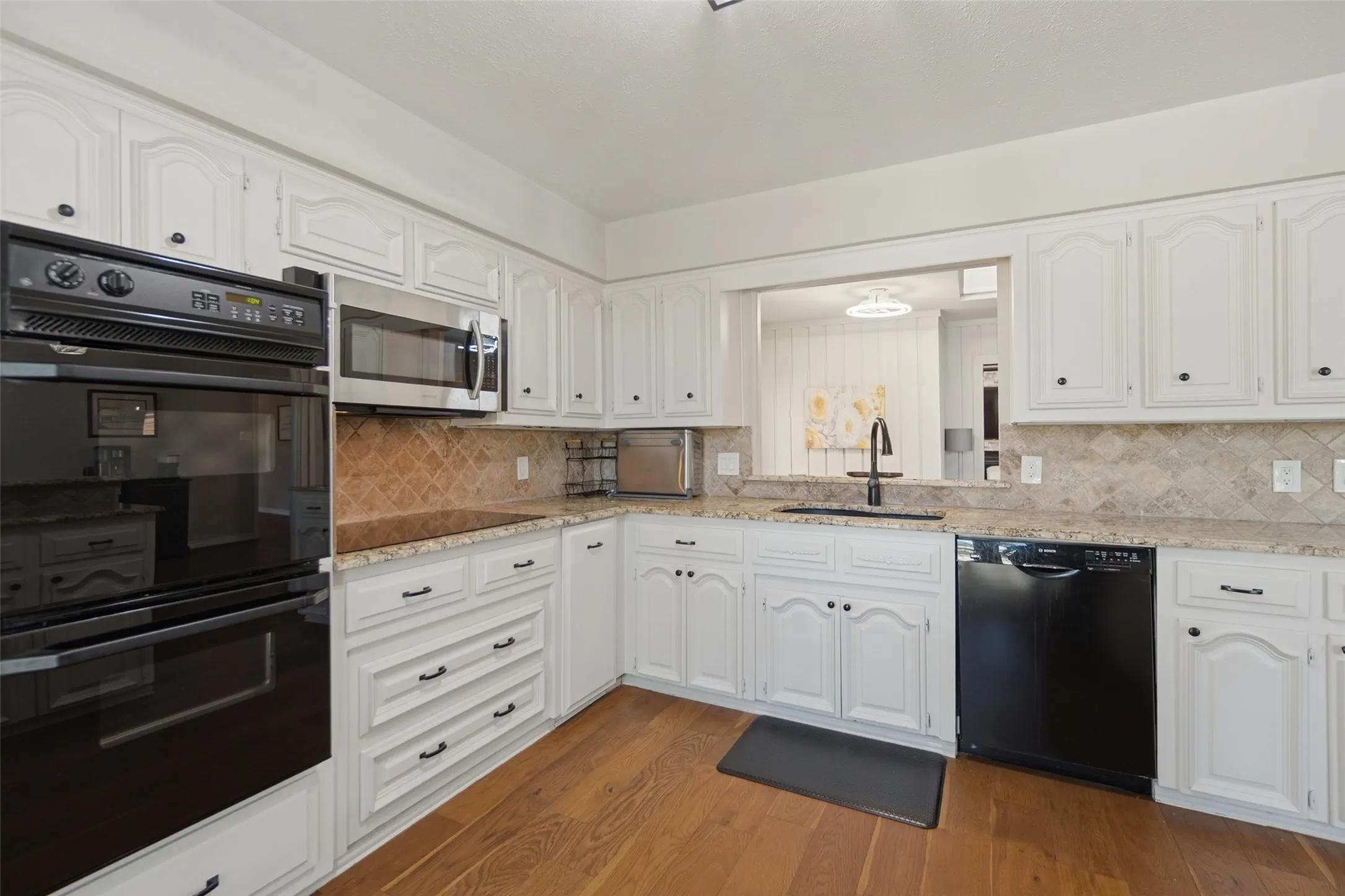 Kitchen featuring white cabinetry, granite countertops, a tiled backsplash, and wood-finish flooring