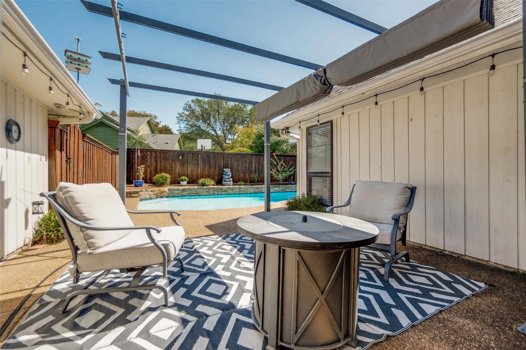 Poolside patio featuring a pergola, string lighting, and wood fencing