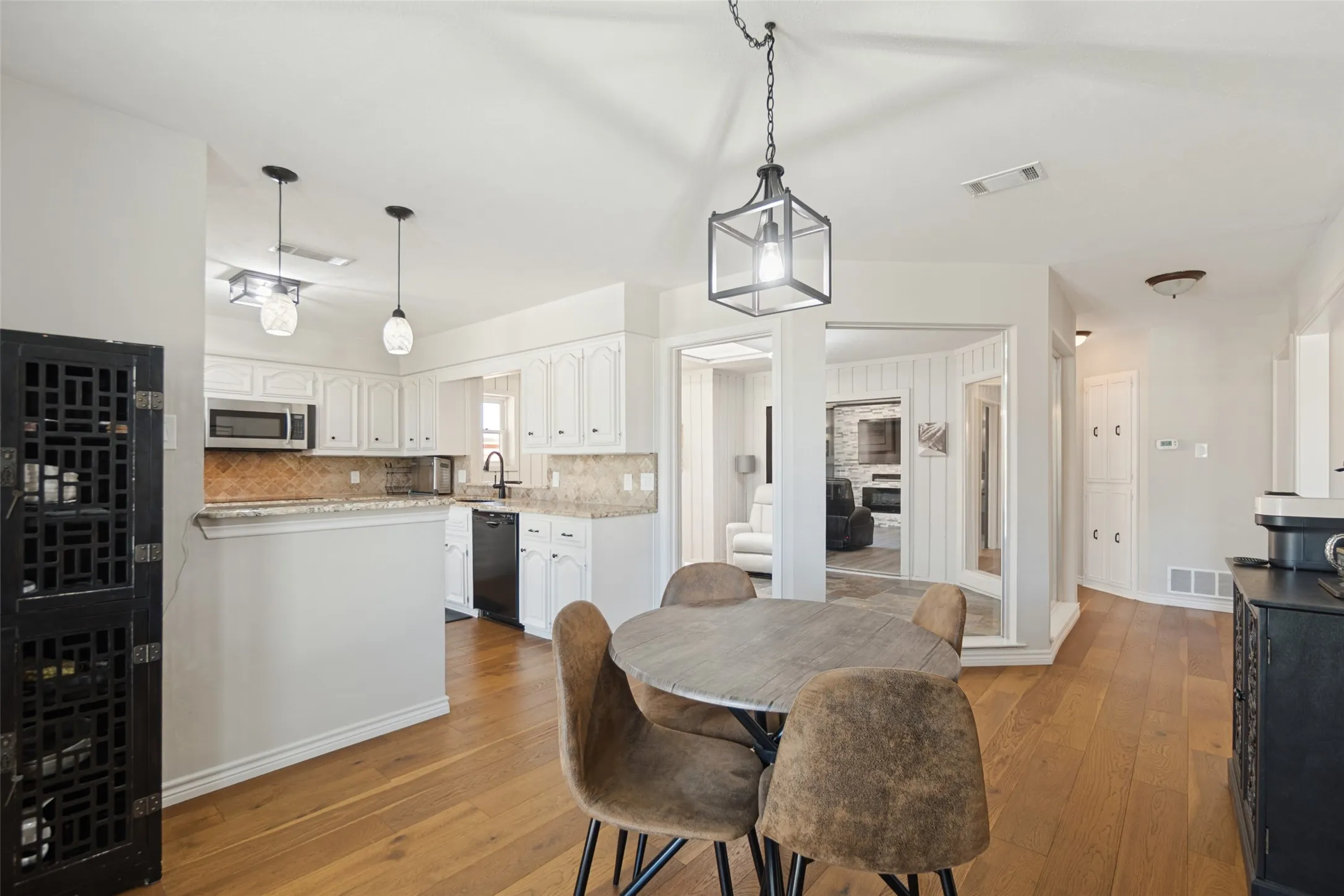 Kitchen featuring white cabinetry, stainless steel microwave, black dishwasher, and a stone-look backsplash