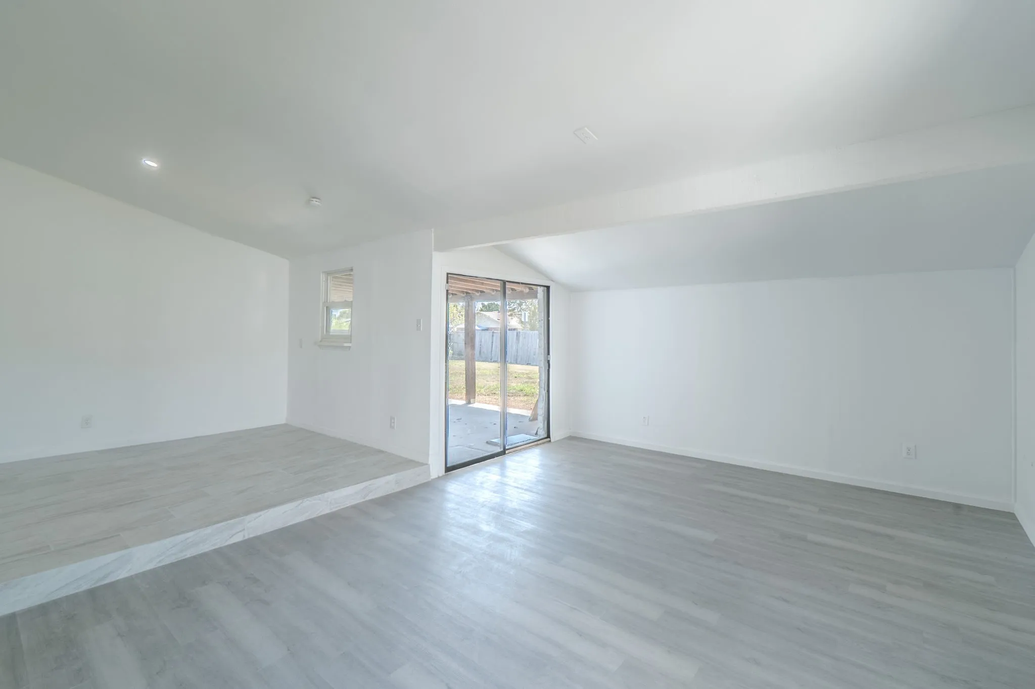 Expansive interior featuring light wood-finish flooring, a raised platform with matching flooring, and a large sliding glass door with exterior access