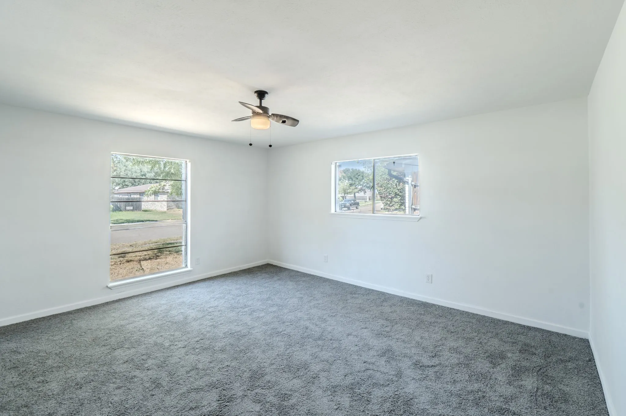 Bright interior space with light-toned walls, dark gray carpeting, and a ceiling fan with integrated lighting