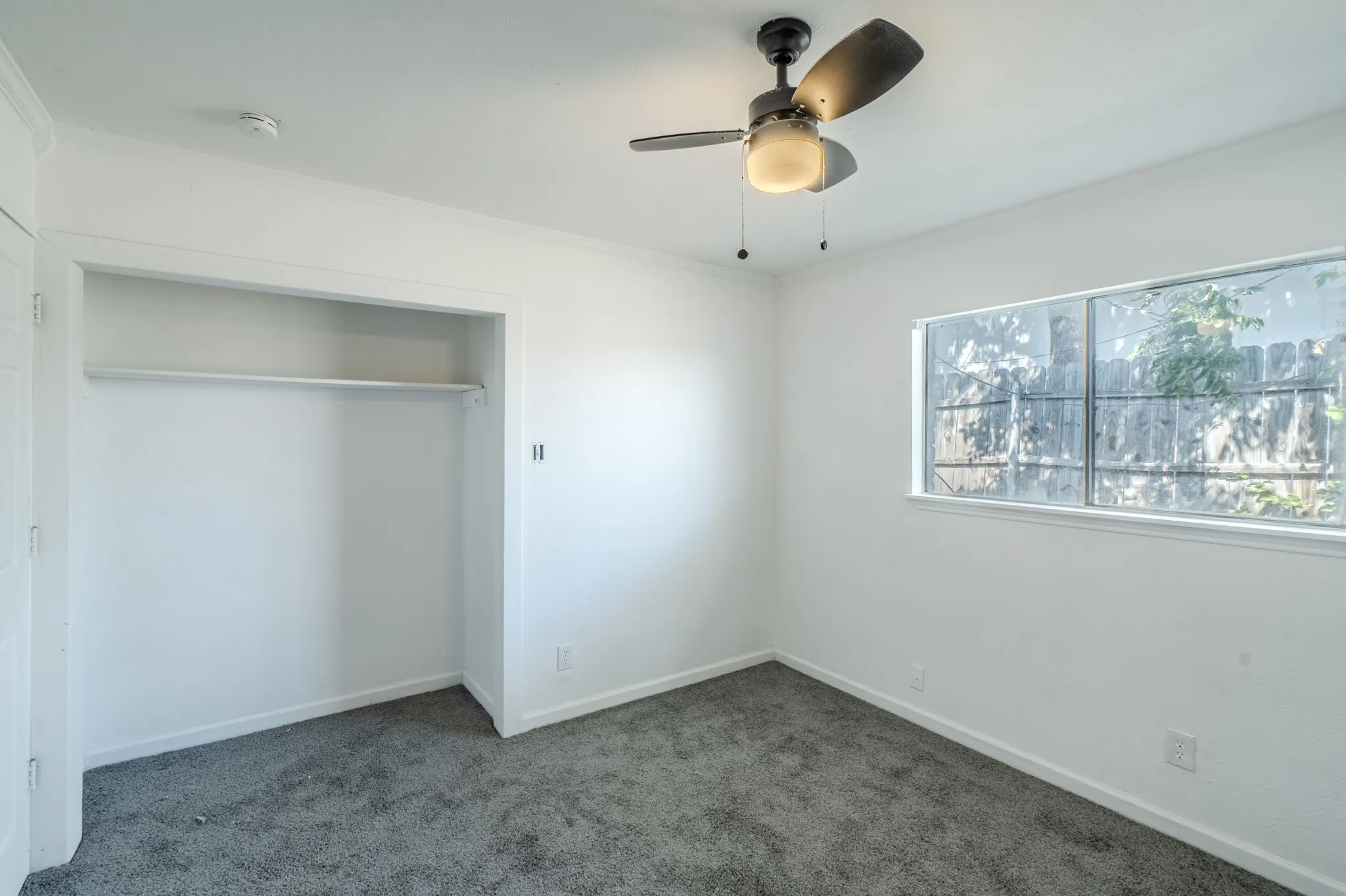 Recessed closet with clothes rod, ceiling fan with integrated lighting, broad window, and carpet flooring
