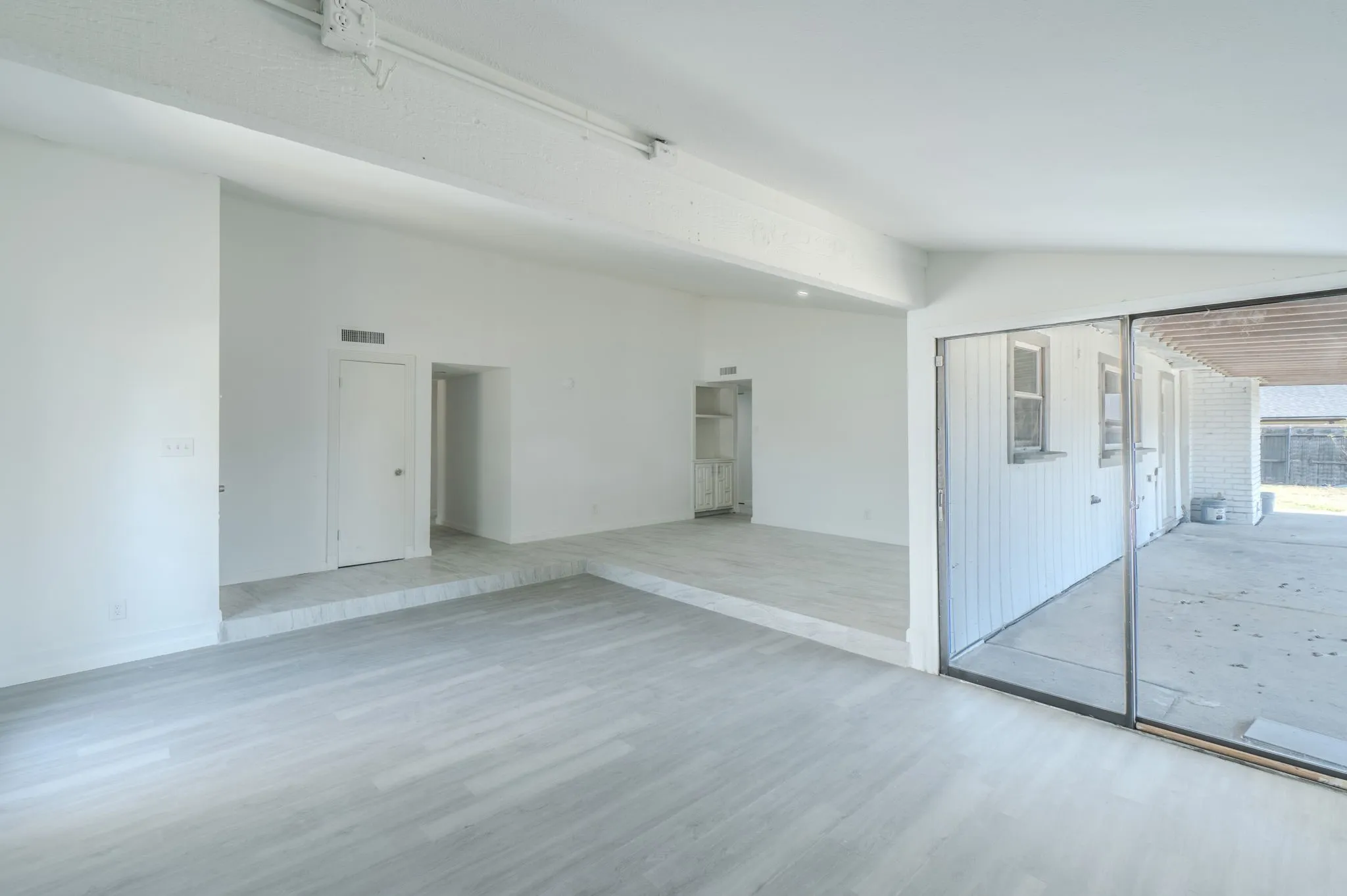 Expansive room featuring wood-finish flooring, white walls, and a raised section with tile flooring