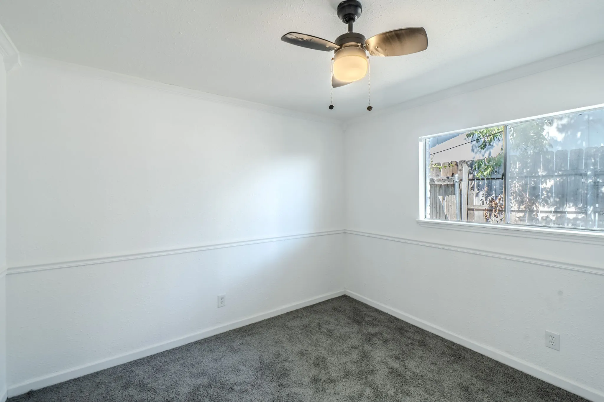 White walls featuring decorative trim, dark gray carpeting, and a ceiling fan with integrated lighting