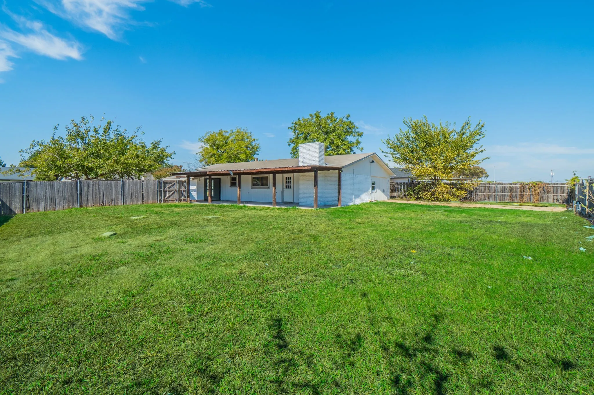 Expansive grassy yard with wood fencing and a covered patio
