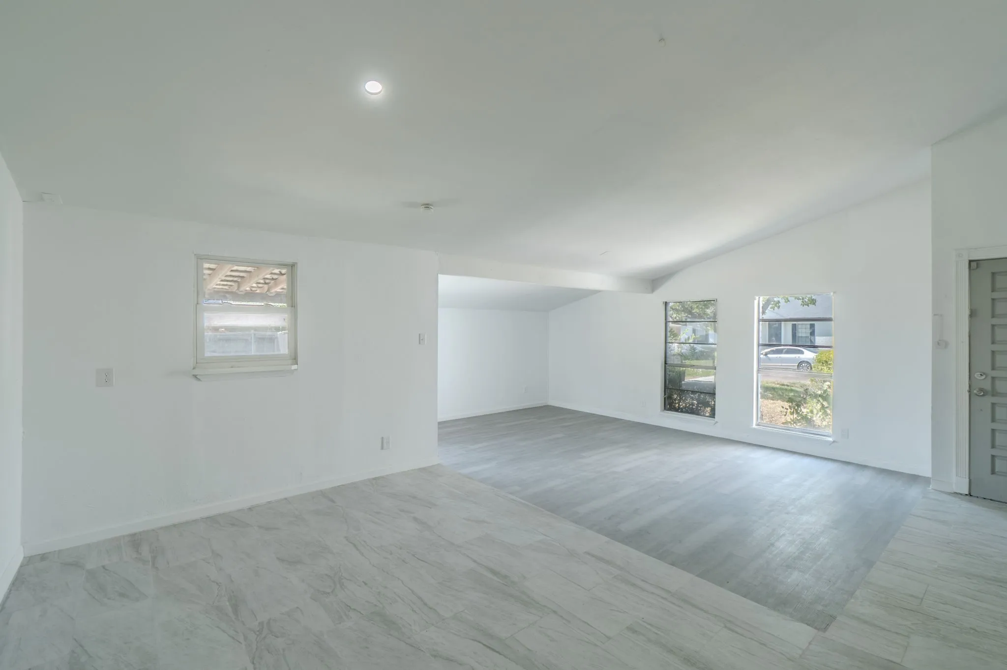 Vaulted ceilings with recessed lighting, large windows, wood-finish flooring, and a paneled entry door