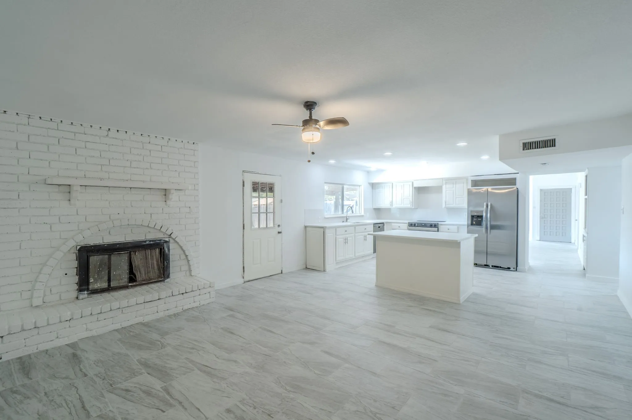 Open-concept living space featuring a white brick fireplace, tile flooring, and a ceiling fan