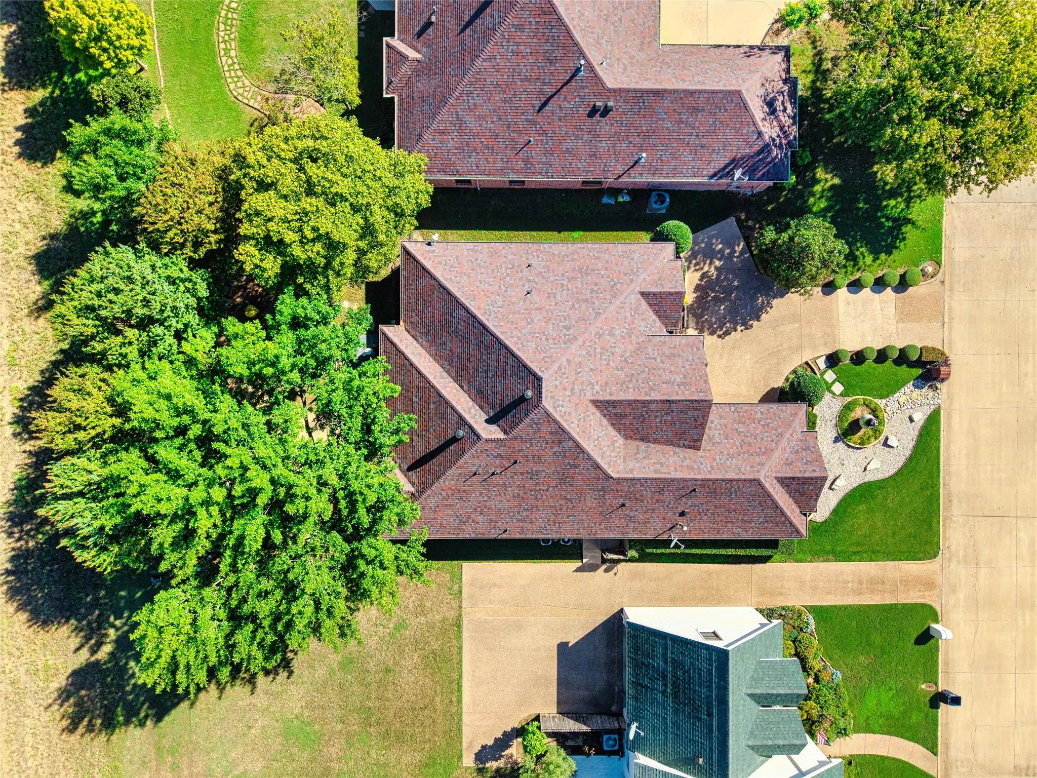 Shingle roofing, mature trees, manicured lawns, and concrete driveways