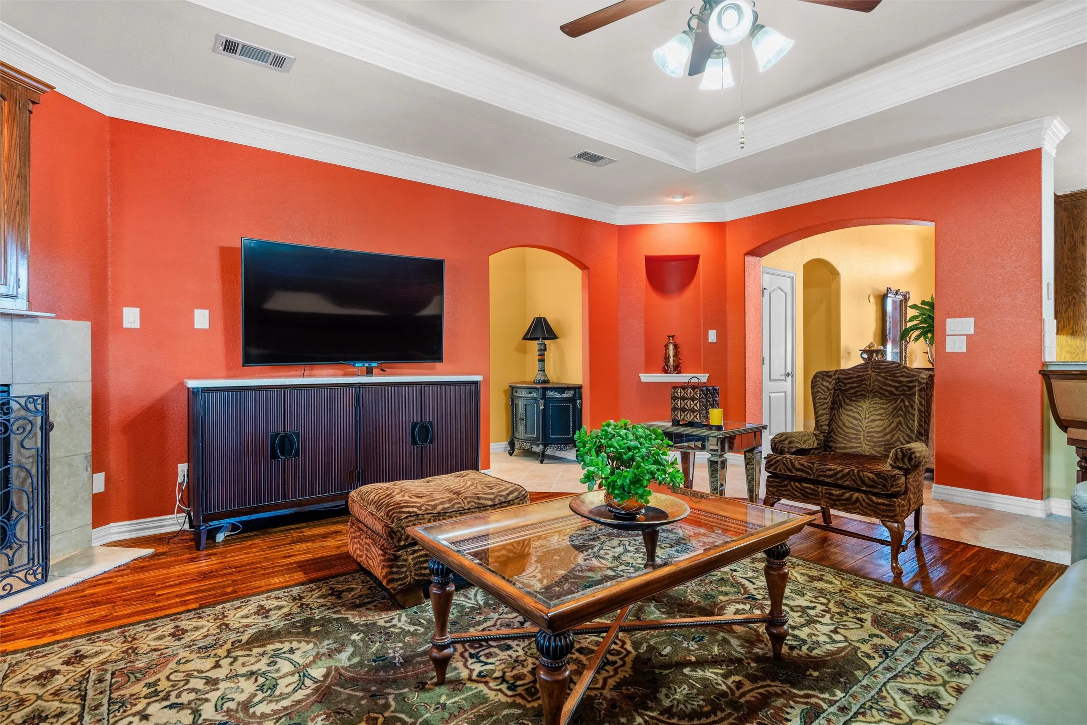 Teak wood-style flooring and arched doorways complement the tray ceiling with a fan light fixture