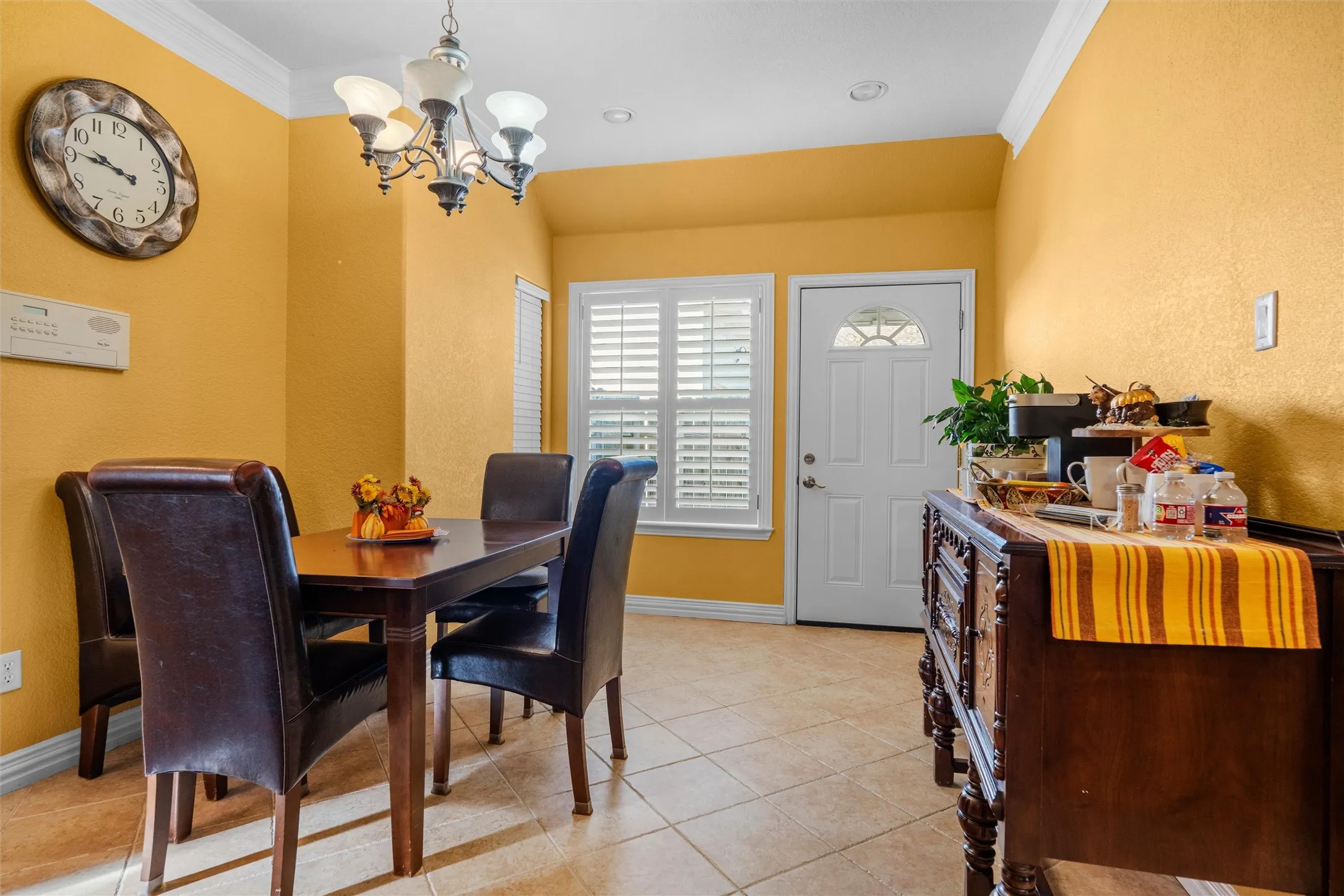 Ceramic tile flooring throughout, featuring a multi-light chandelier, a window with plantation shutters, and a white entry door with an arched glass insert