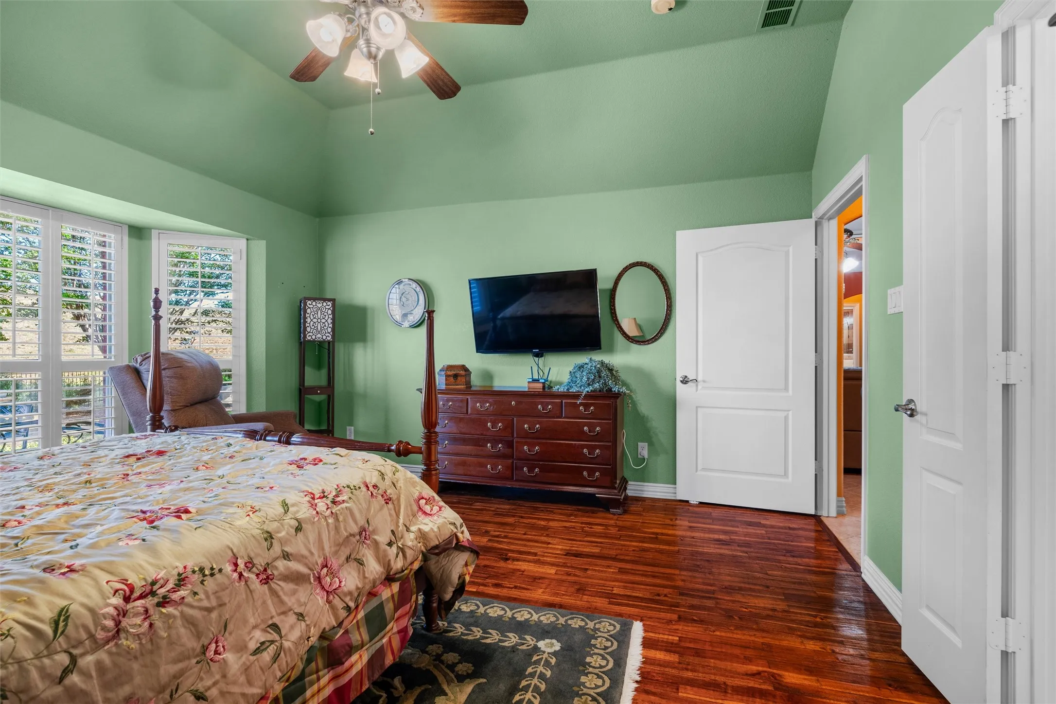 Primary Bedroom vaulted ceiling with a ceiling fan, bay windows with plantation shutters, Teak wood flooring, and white interior doors