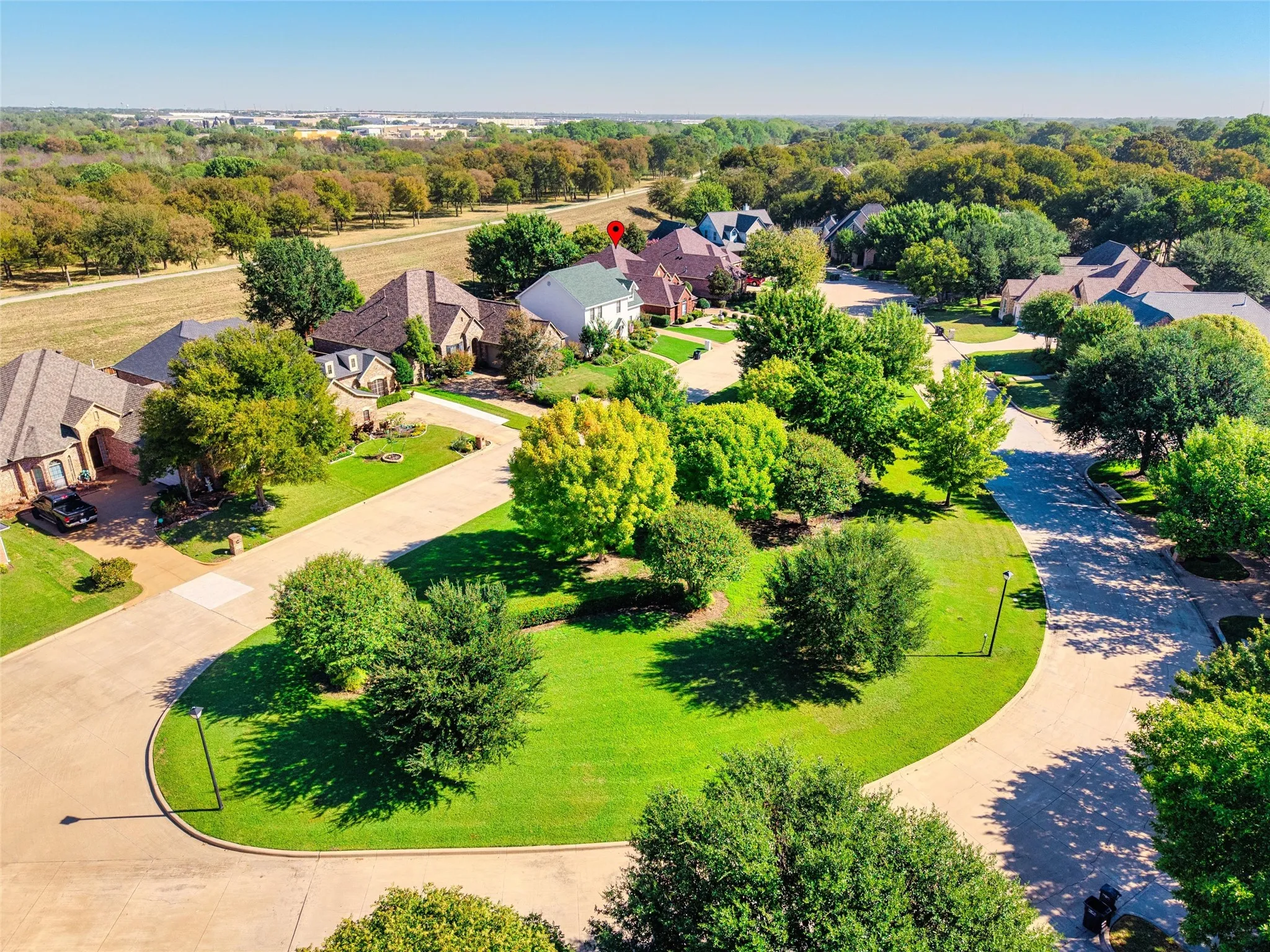 Residential neighborhood featuring mature trees, paved streets, and a manicured green space and park with sitting area across the street